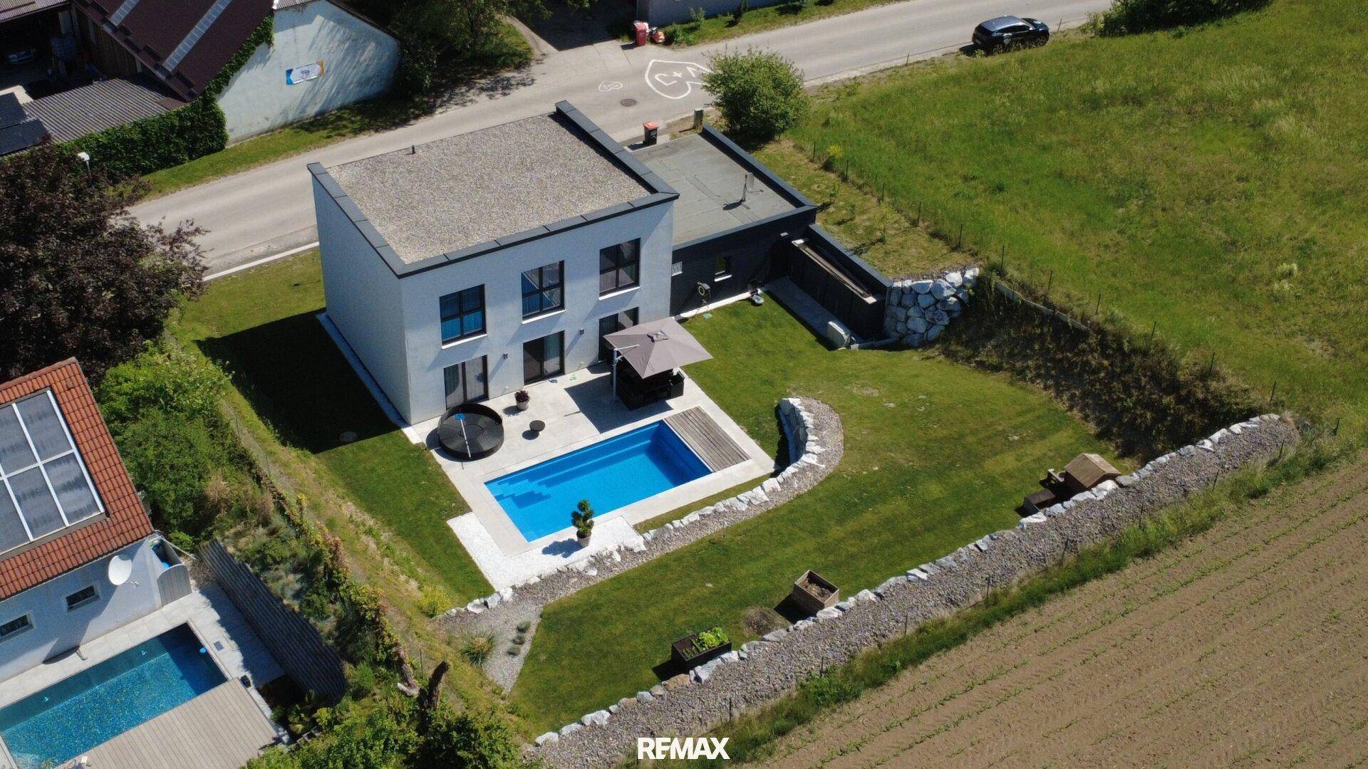 Luftaufnahme eines modernen Hauses mit Pool und großem Garten, umgeben von Grünflächen.