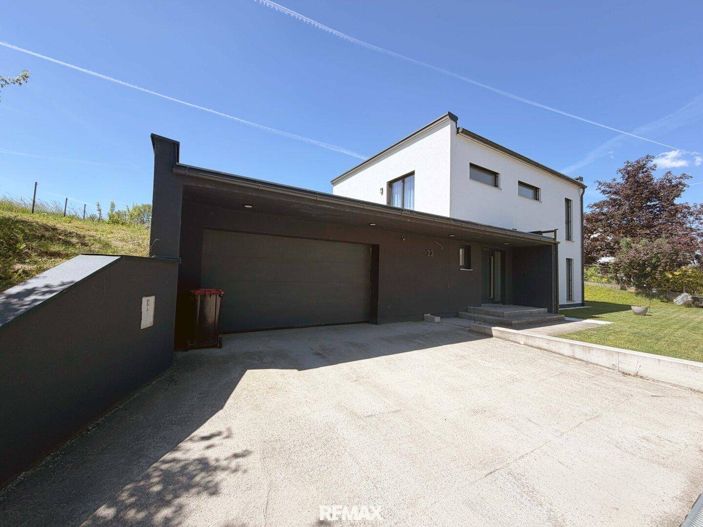 Moderne Hausfassade mit integrierter Garage und Zufahrt, umgeben von Grünflächen.