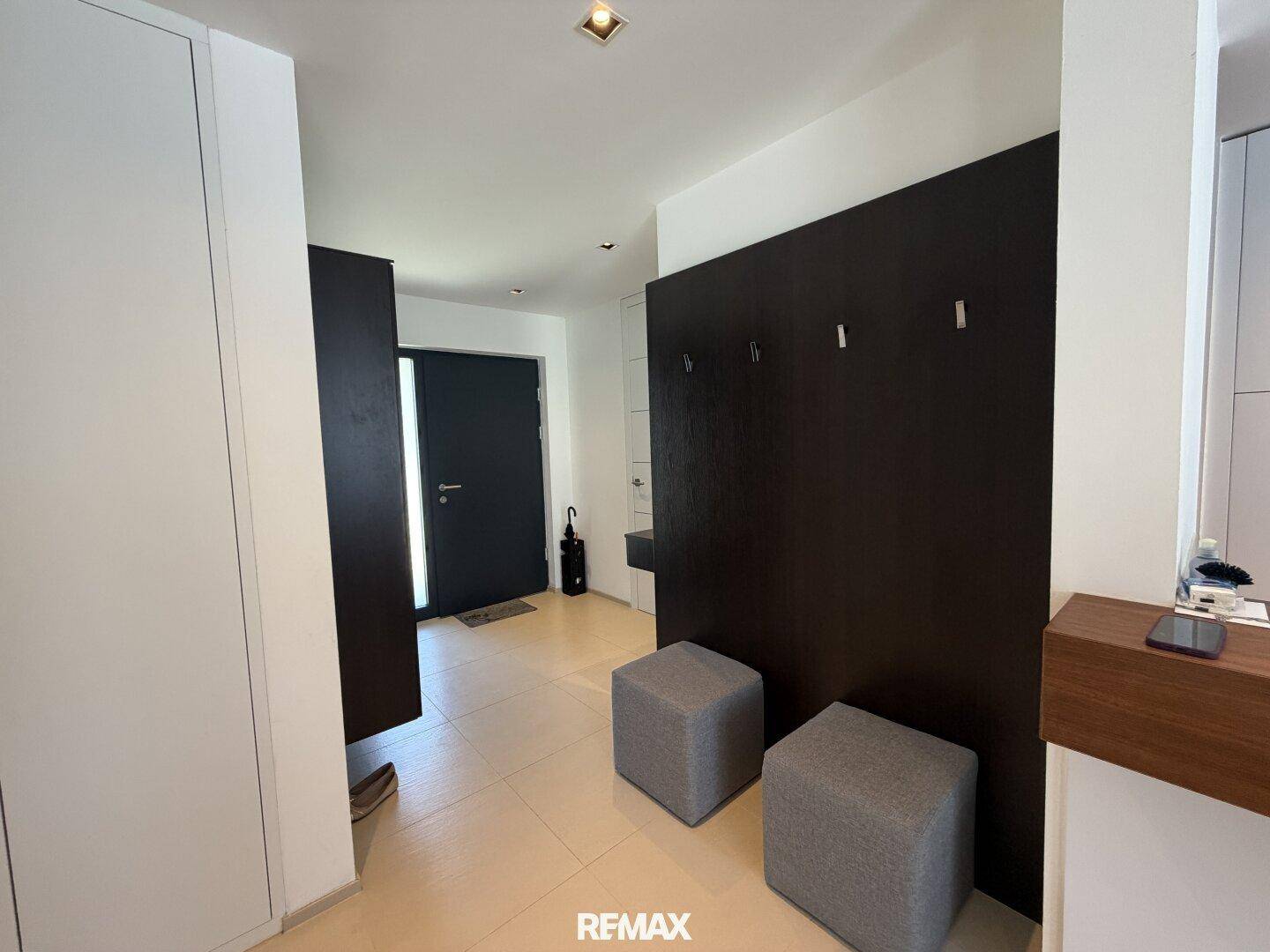 Heller Eingangsbereich mit modernen Fliesen, dunkler Garderobe und schlichten Möbeln.