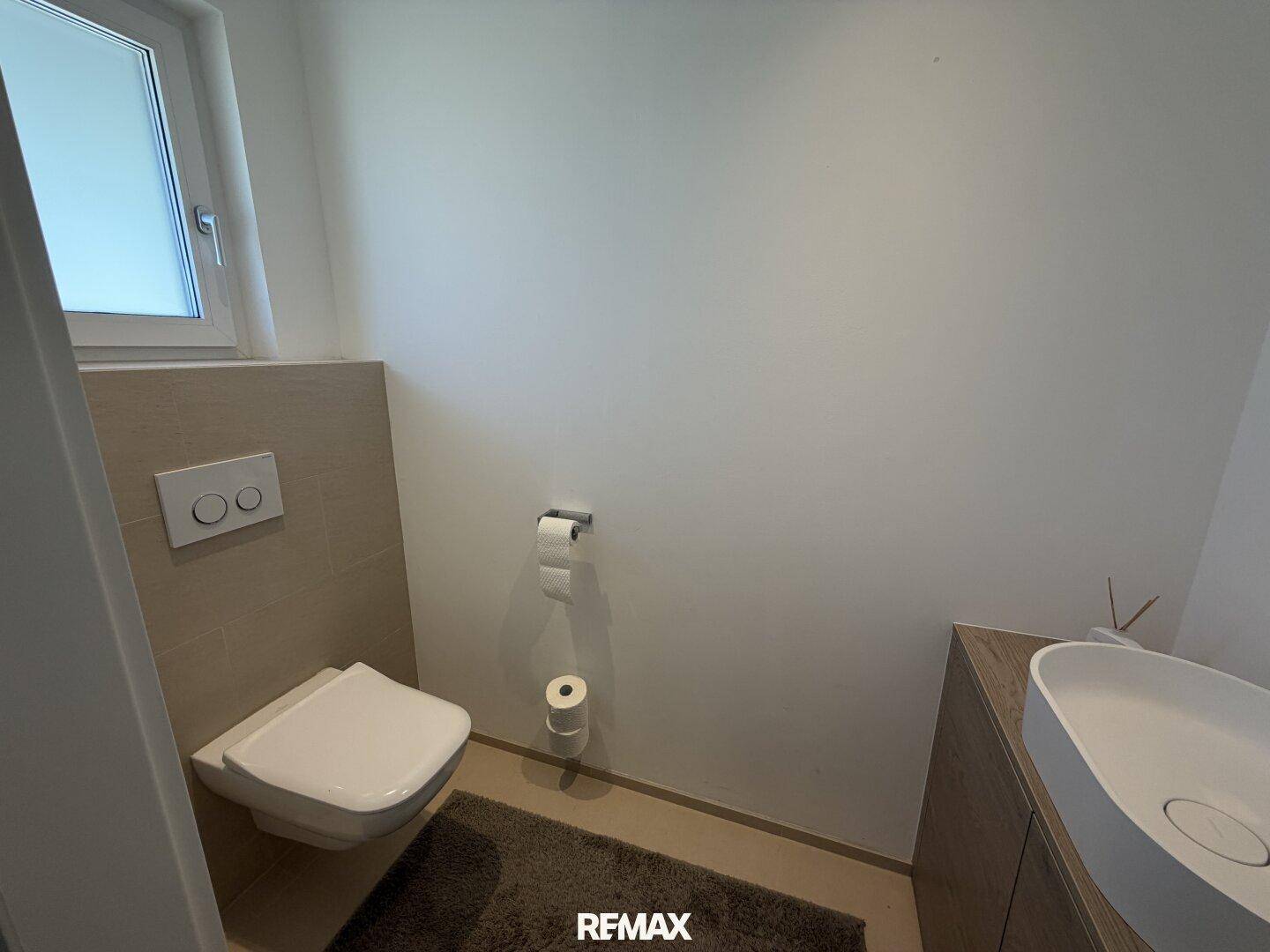 Modernes Gäste-WC mit wandhängender Toilette, kleinem Waschbecken und Fenster für Tageslicht.