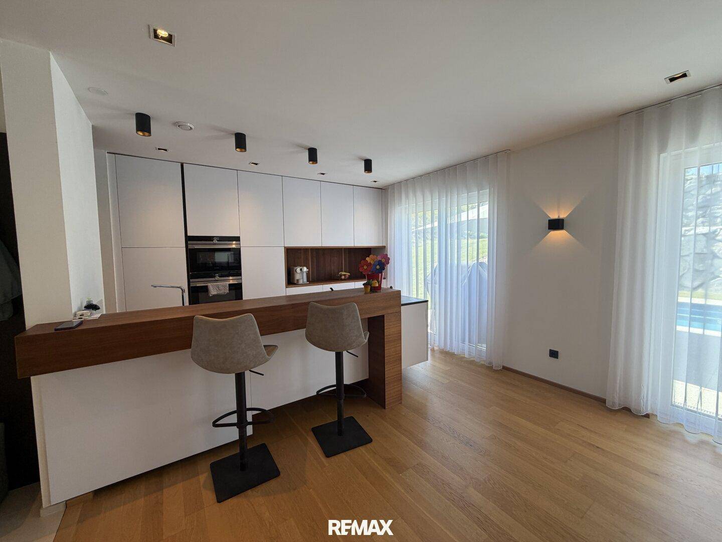 Moderne Küche mit Frühstücksbar, Hockern und Zugang zum Außenbereich durch große Fenster.