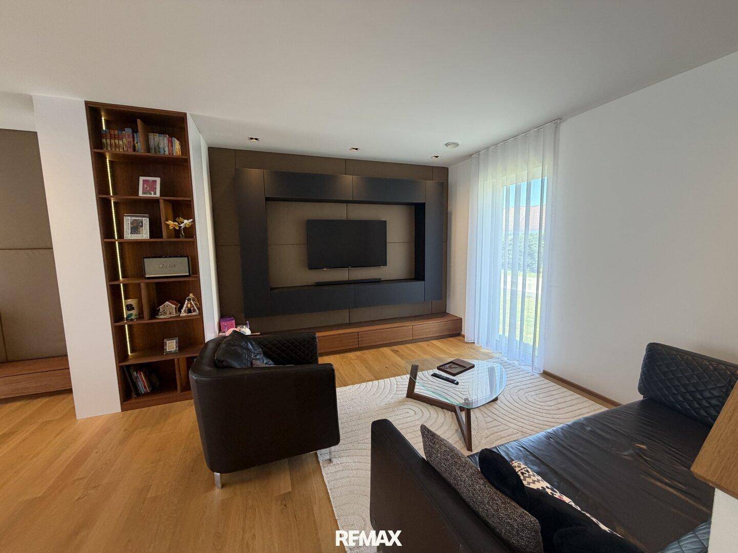 Gemütliches Wohnzimmer mit Holzboden, dunklen Ledermöbeln und integriertem TV-Bereich.