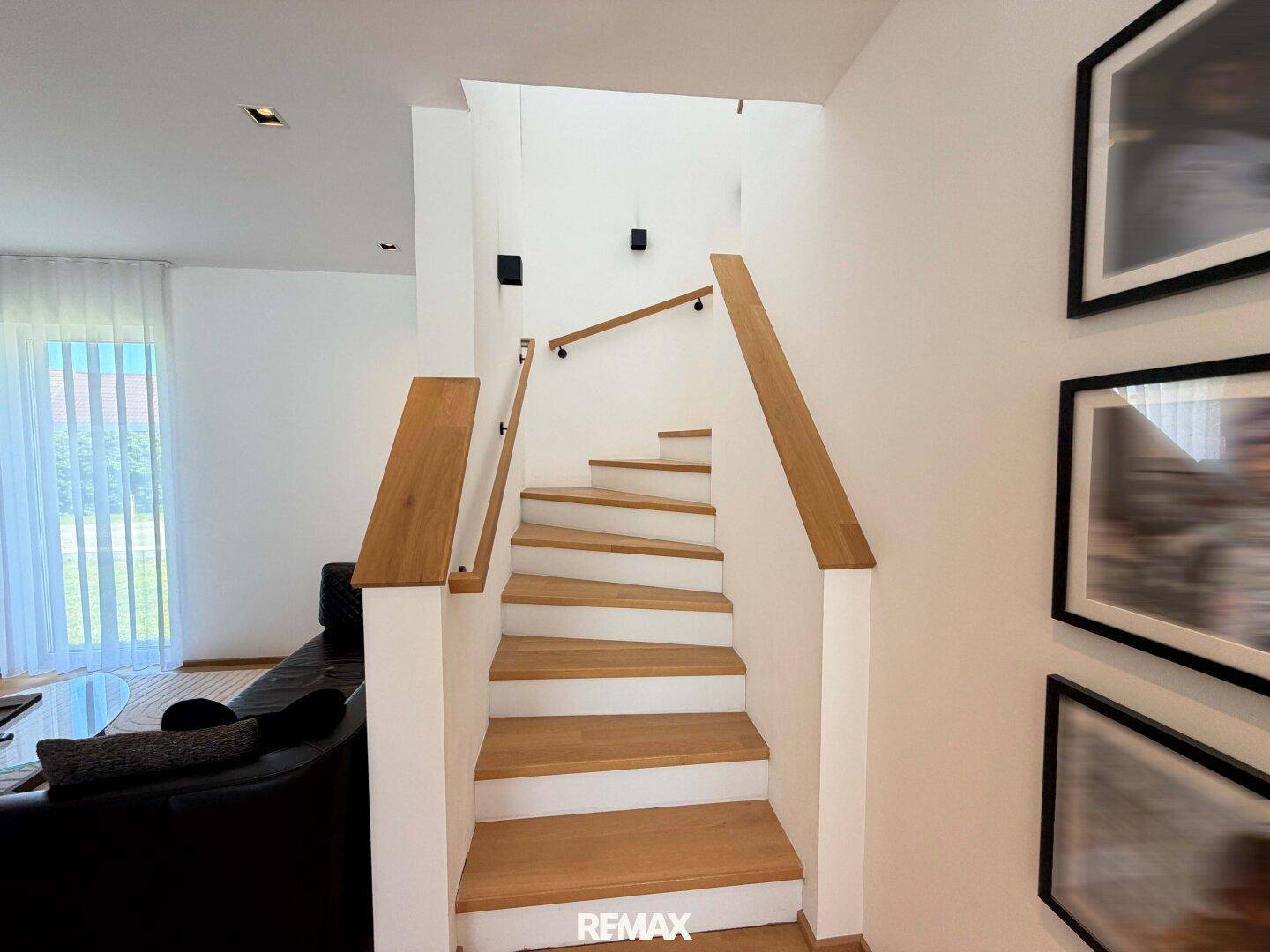 Moderne Holztreppe mit weißem Geländer, die die verschiedenen Ebenen des Hauses verbindet.
