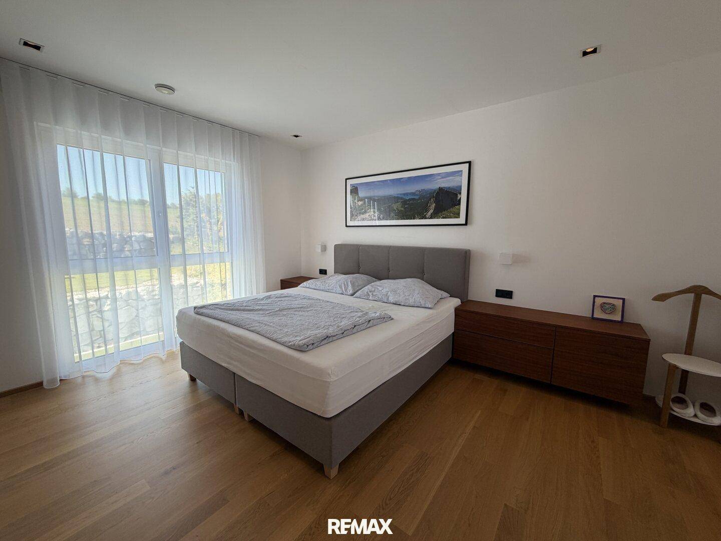 Geräumiges Schlafzimmer mit Doppelbett, Holzboden und großen Fenstern mit Blick ins Grüne.