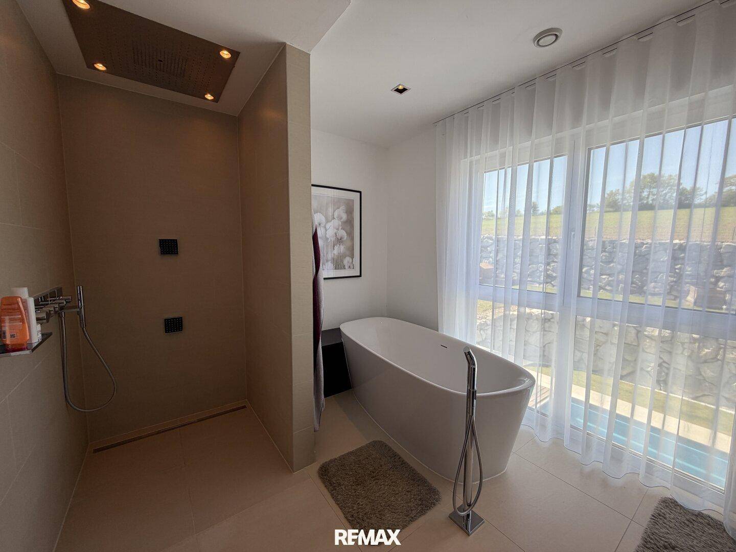 Modernes Badezimmer mit freistehender Badewanne, großer Dusche und Fenster mit Poolblick.