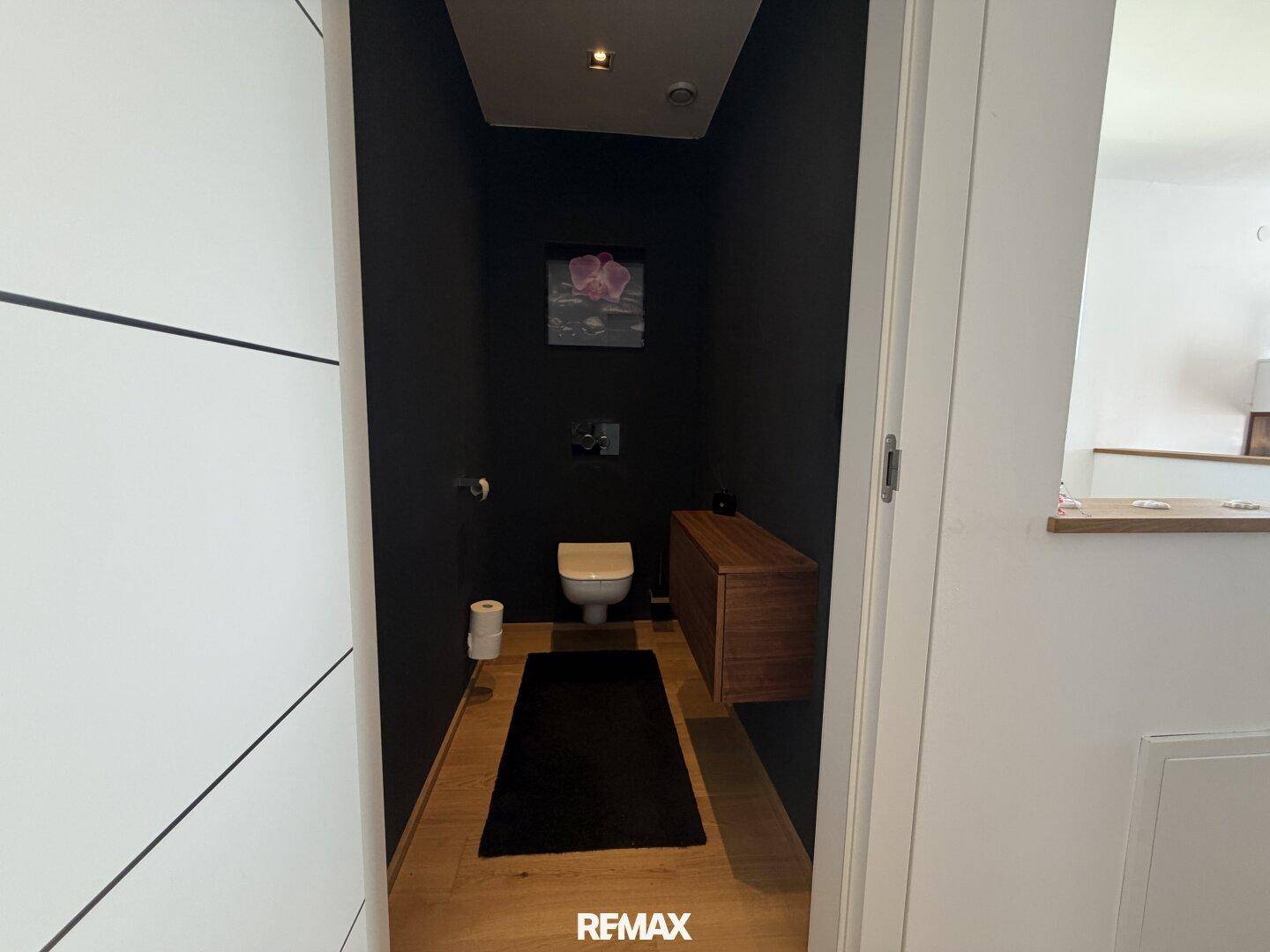 Stilvolles Gäste-WC mit dunklen Wänden, wandhängender Toilette und Holzelementen.