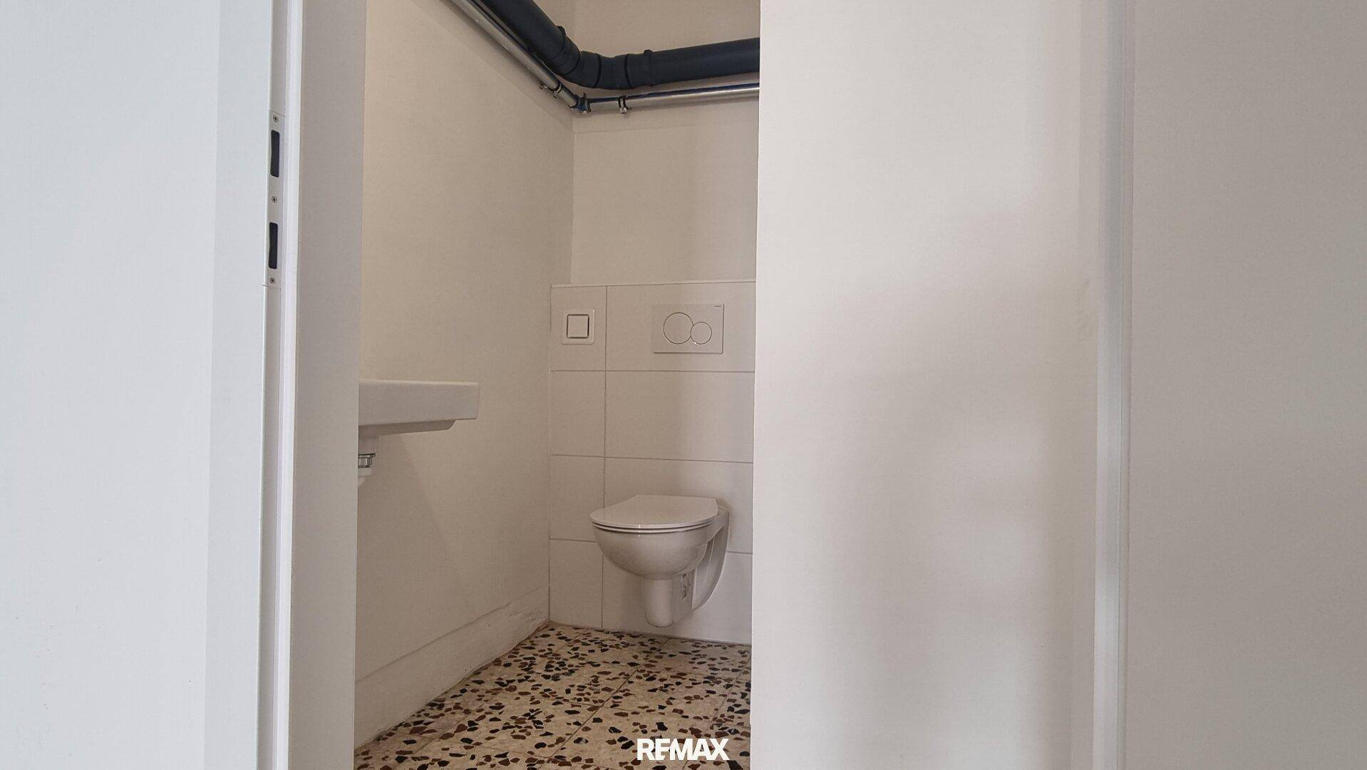 Kleines Gäste-WC mit Wand-WC und Waschbecken, ausgestattet mit Fliesenboden.