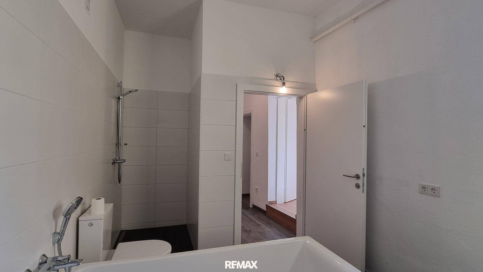 Helles Badezimmer mit Badewanne, Dusche und WC, ausgestattet mit weißen Fliesen.