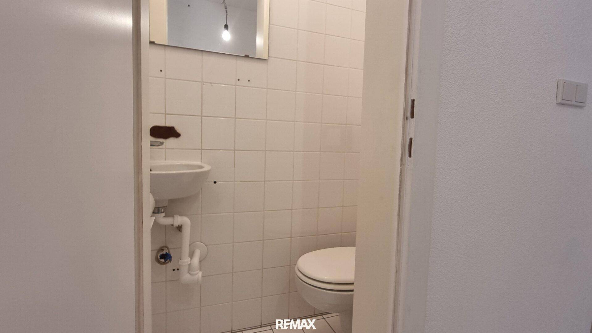 Kleines Gäste-WC mit Waschbecken und Toilette, hell gefliest und funktional.