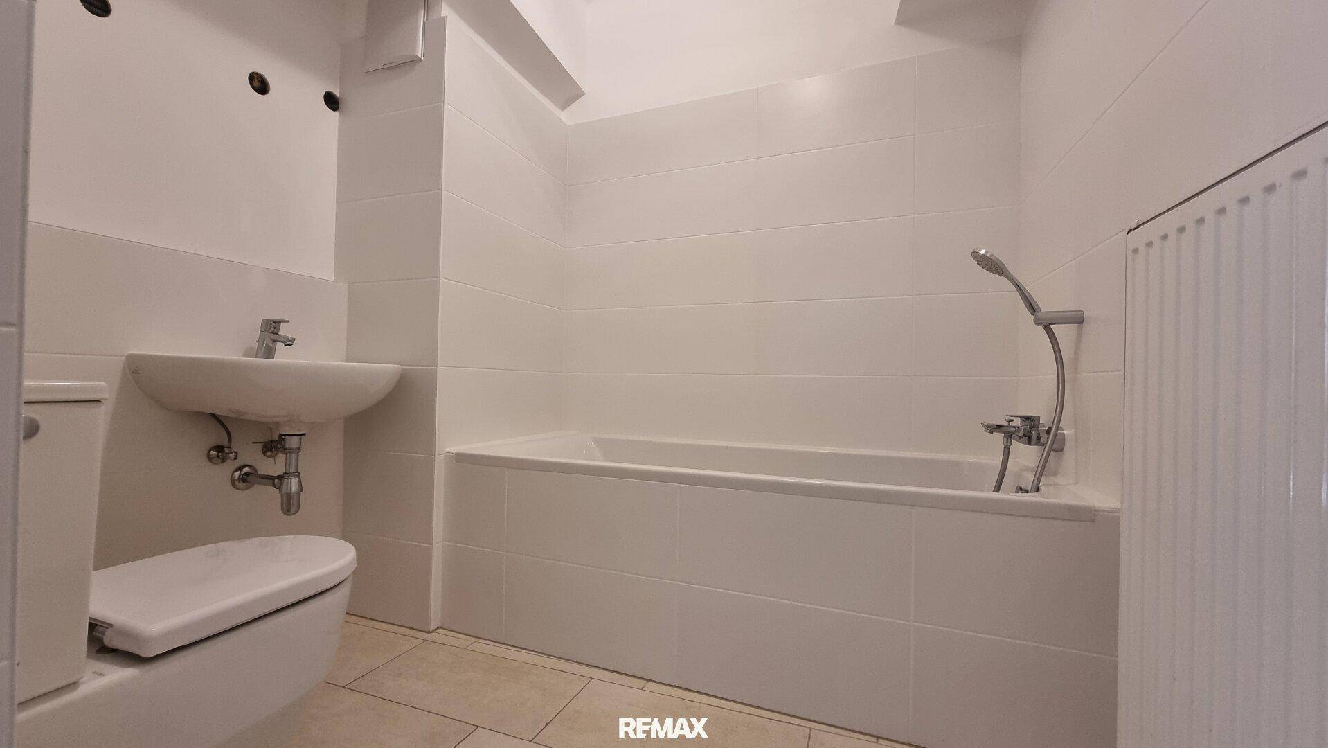 Badezimmer mit Badewanne, WC und Waschbecken, hell gefliest und funktional eingerichtet.