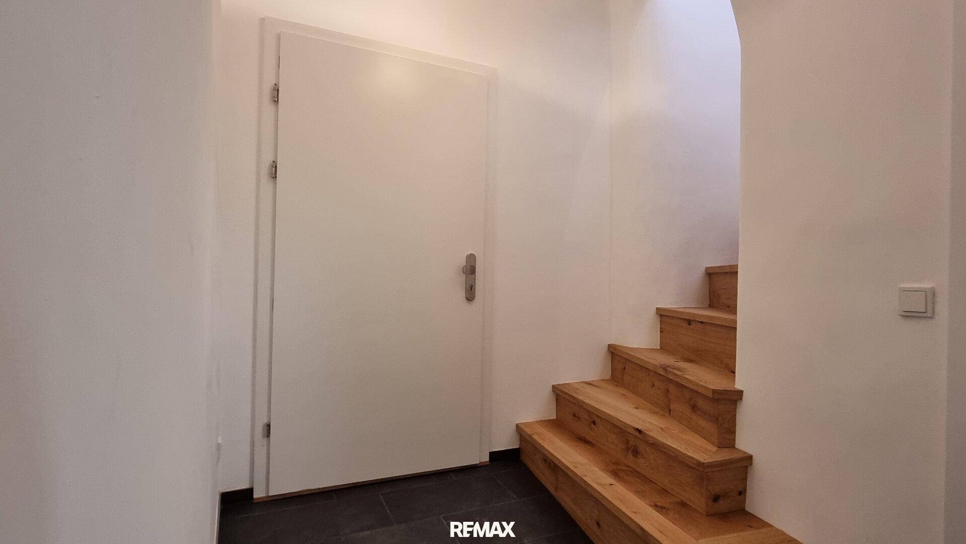 Heller Treppenaufgang mit Holzstufen und weißer Tür, führt zu den oberen Etagen.