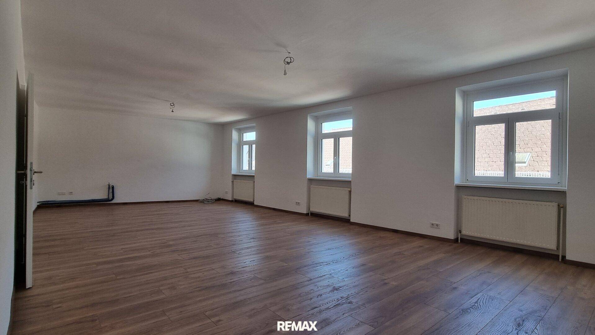 Helles, leeres Zimmer mit Laminatboden und mehreren Fenstern, bereit zur individuellen Gestaltung.