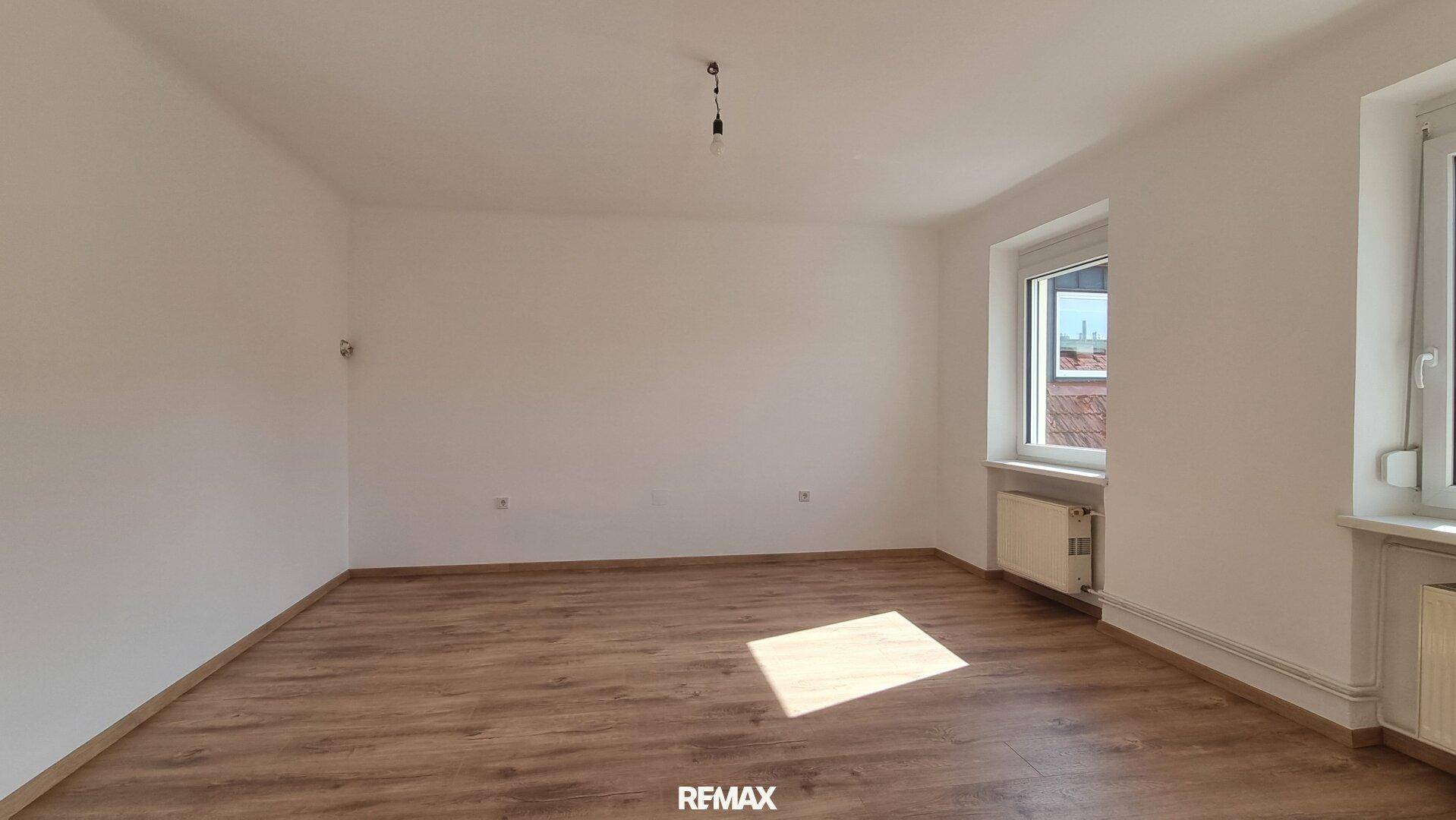 Heller Raum mit Laminatboden und einem Fenster, das viel Tageslicht hereinlässt.