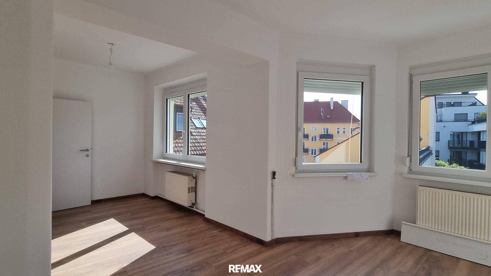 Geräumiger, heller Raum mit mehreren Fenstern und Laminatboden, bereit zur Einrichtung.