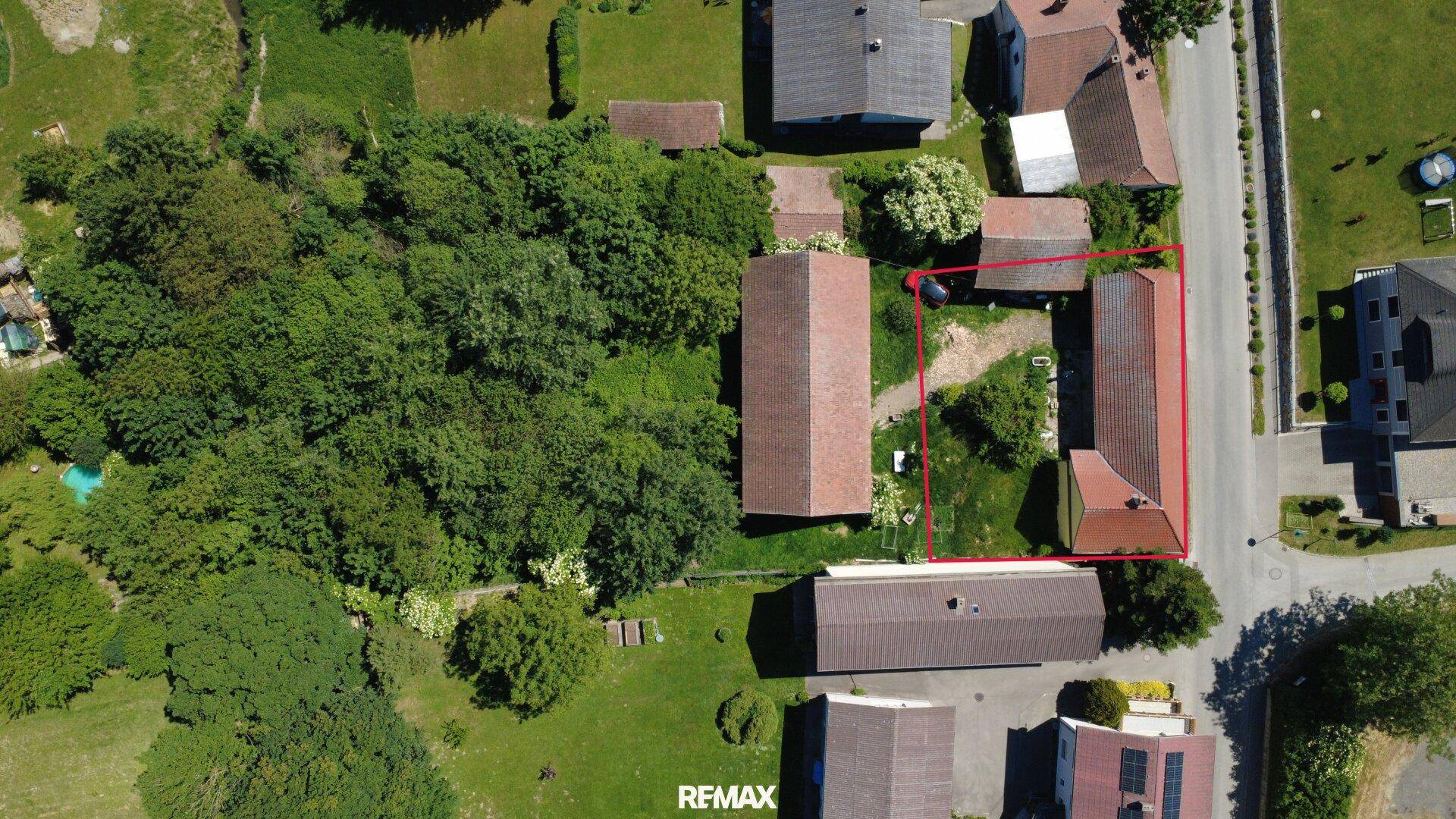 Vogelperspektive des Grundstücks mit zwei Gebäuden und viel Grünfläche, umrandet in Rot.