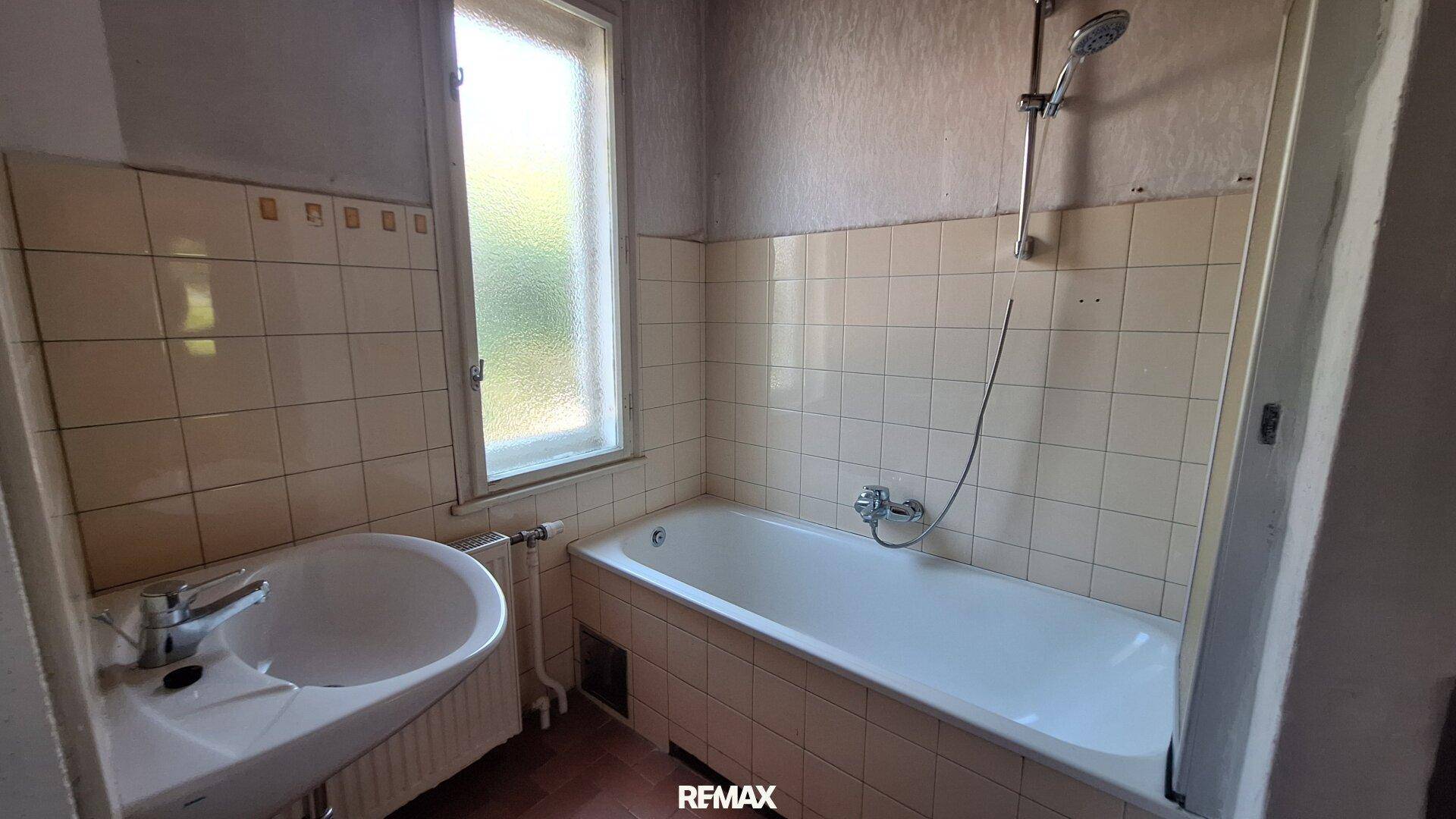 Badezimmer mit Badewanne, Waschbecken und hellen Fliesen, ausgestattet mit einem Fenster.