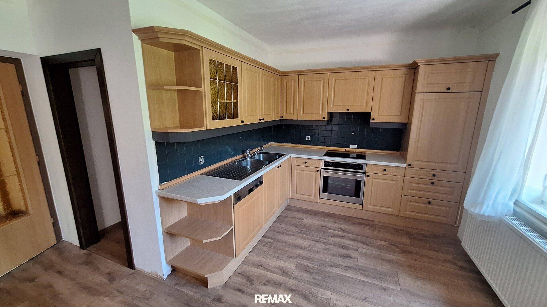 Helle Holzküche mit Einbaugeräten, dunklem Fliesenspiegel und praktischer Theke.