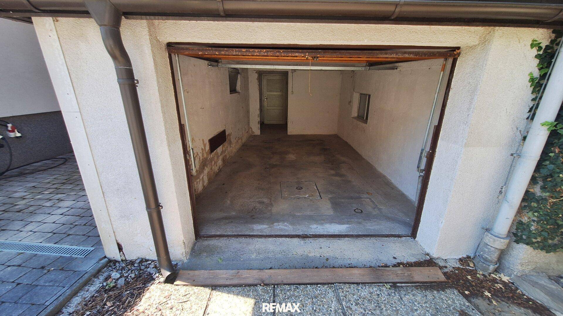 Leere Garage mit Betonboden und einem kleinen Fenster, bereit zur Nutzung.
