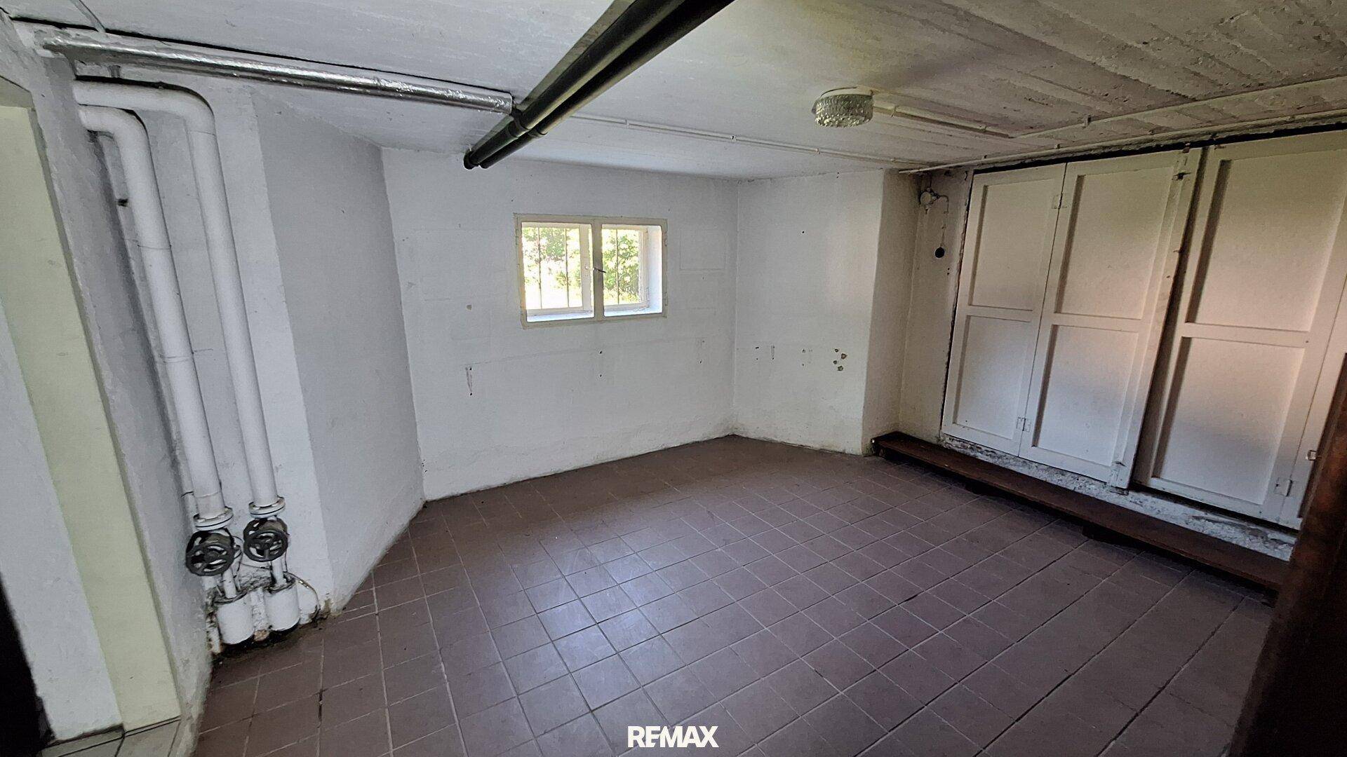 Geräumiger Kellerraum mit Fliesenboden, Fenster und praktischen Einbauschränken.