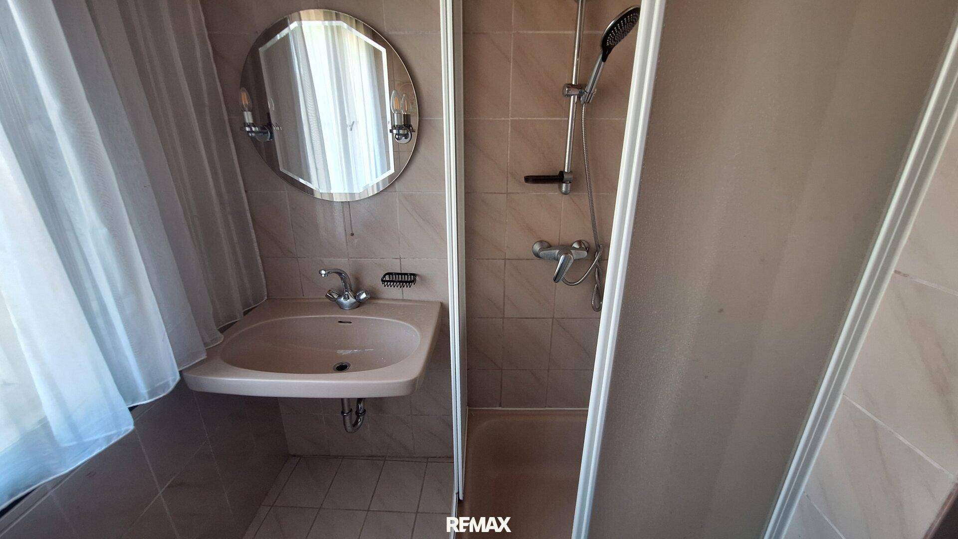 Kleines Badezimmer mit Waschbecken, Duschkabine und einem runden Spiegel.