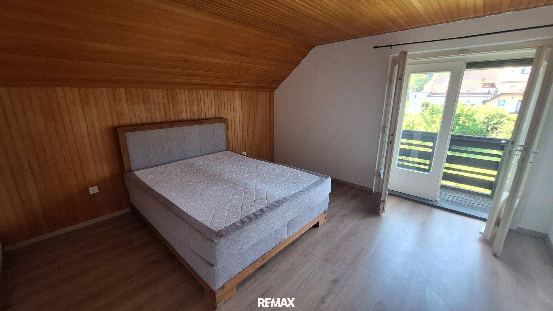 Schlafzimmer mit Holztäfelung, Bett und Doppeltüren, die zu einem Balkon führen.