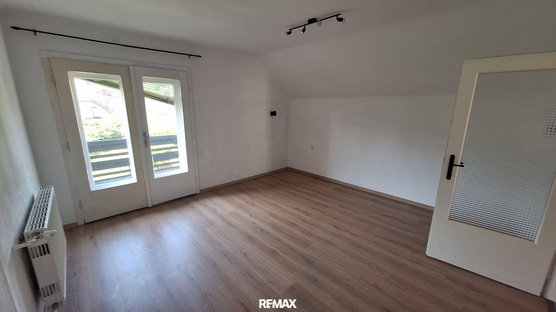 Heller Raum mit Laminatboden und Balkonzugang durch Doppeltüren.