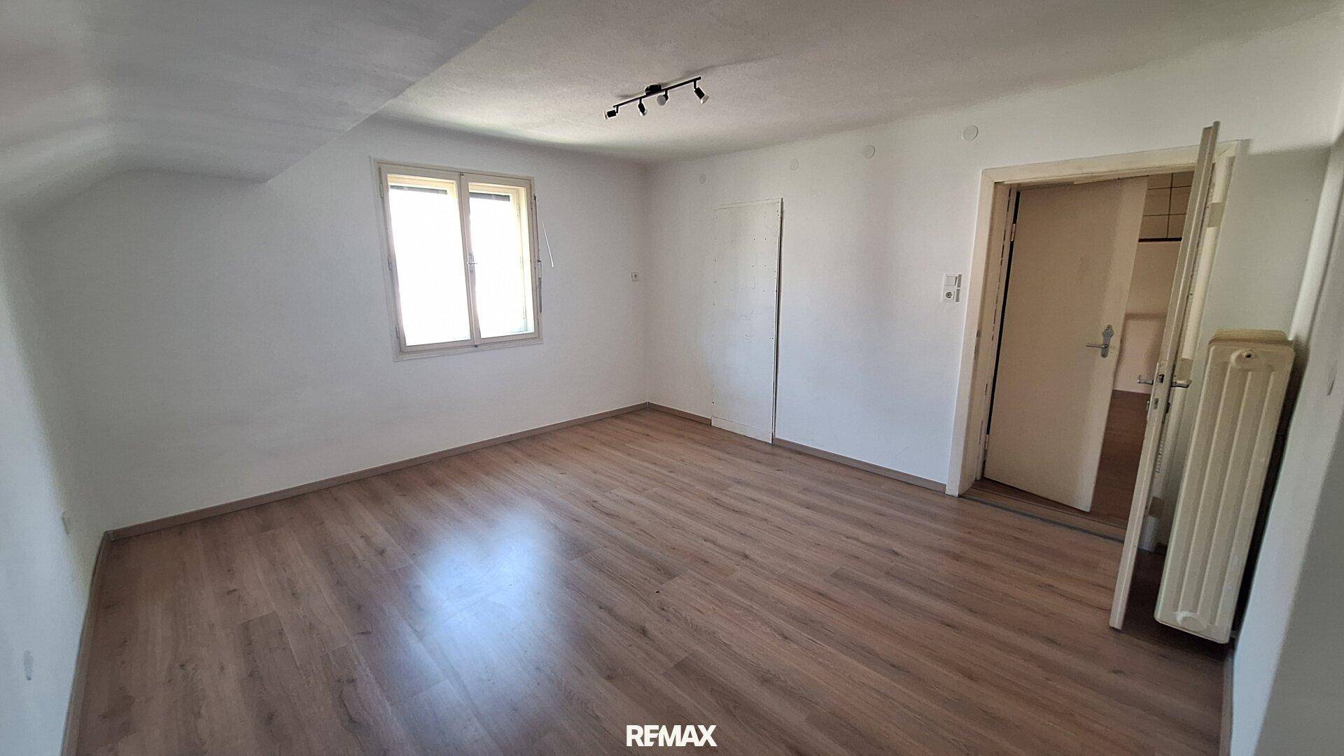 Heller Raum mit Laminatboden, Fenster und Heizkörper, vielseitig nutzbar.