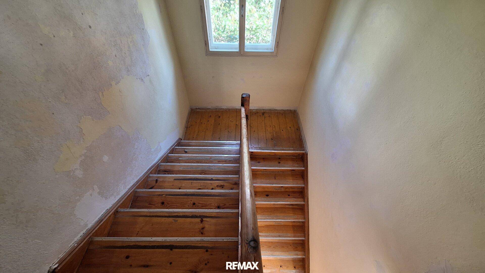 Holztreppe mit Geländer und einem kleinen Fenster im oberen Bereich.