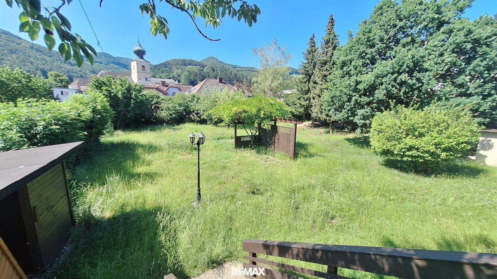 Großer Garten mit Rasenfläche und Blick auf das nahegelegene Dorf mit Kirchturm.