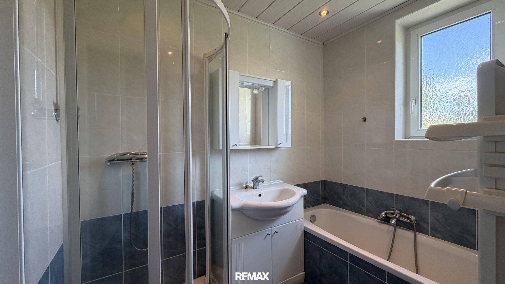 Badezimmer mit Badewanne, Duschkabine, Waschbecken und Fenster.