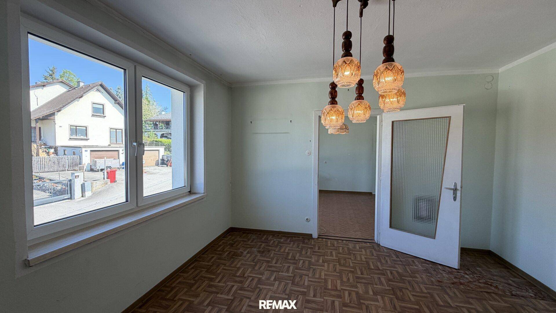 Zimmer mit Laminatboden, großen Fenstern und Blick auf die Nachbarschaft.
