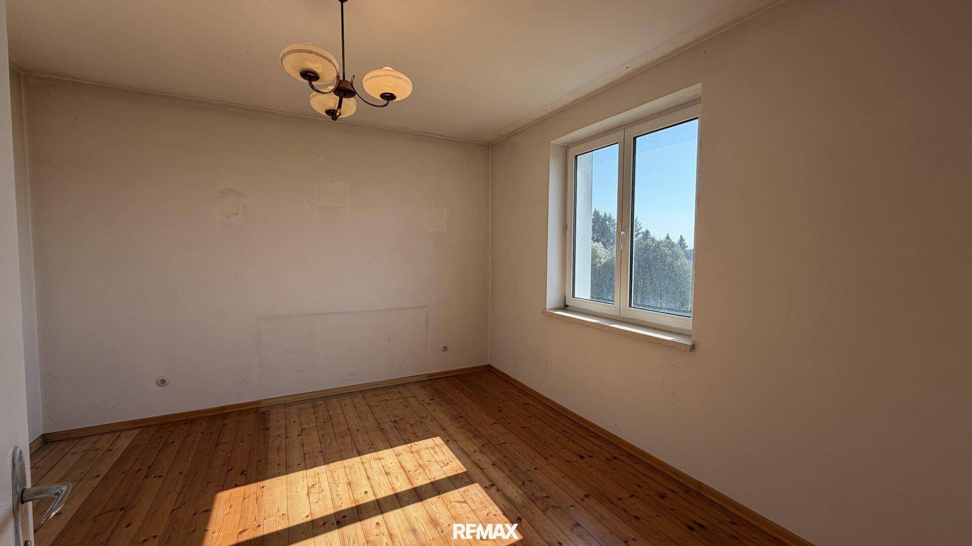 Schlafzimmer mit Holzdielenboden und großem Fenster für viel Tageslicht.
