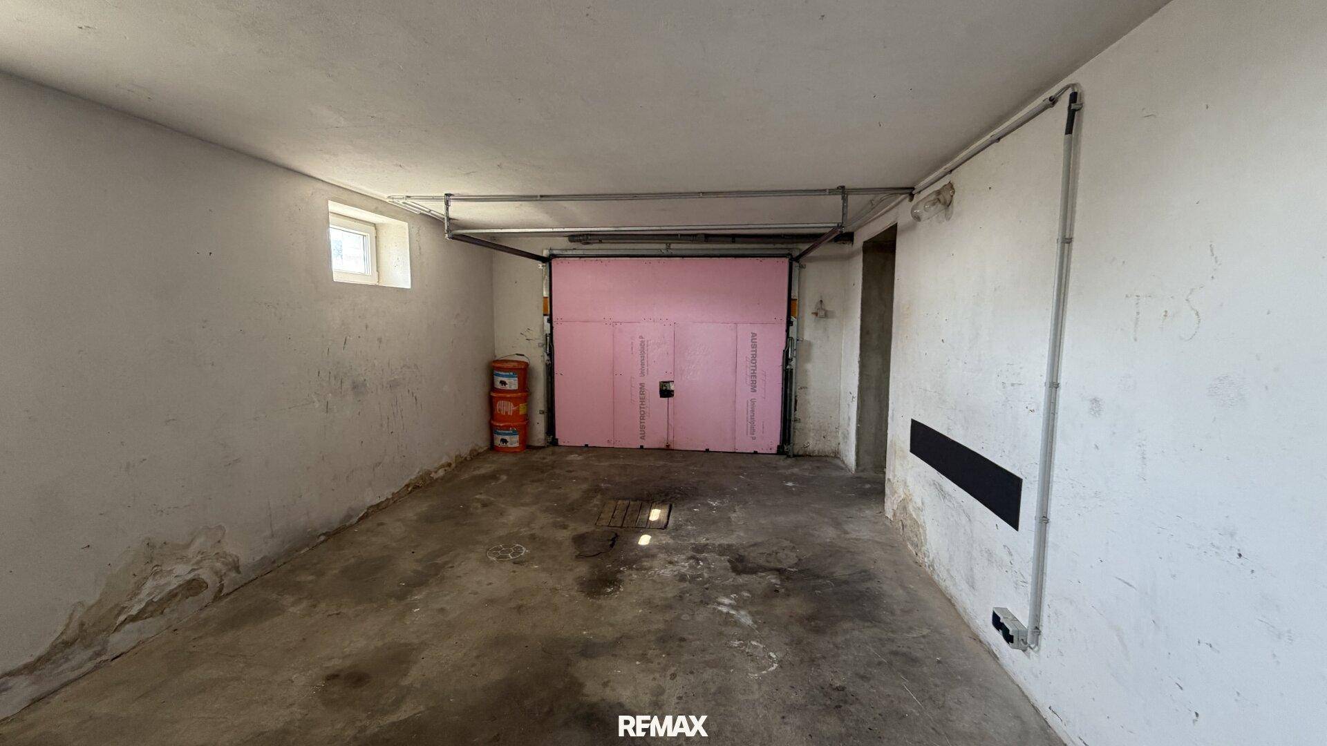 Geräumige Garage im Untergeschoss mit rosa Garagentor und Betonboden.