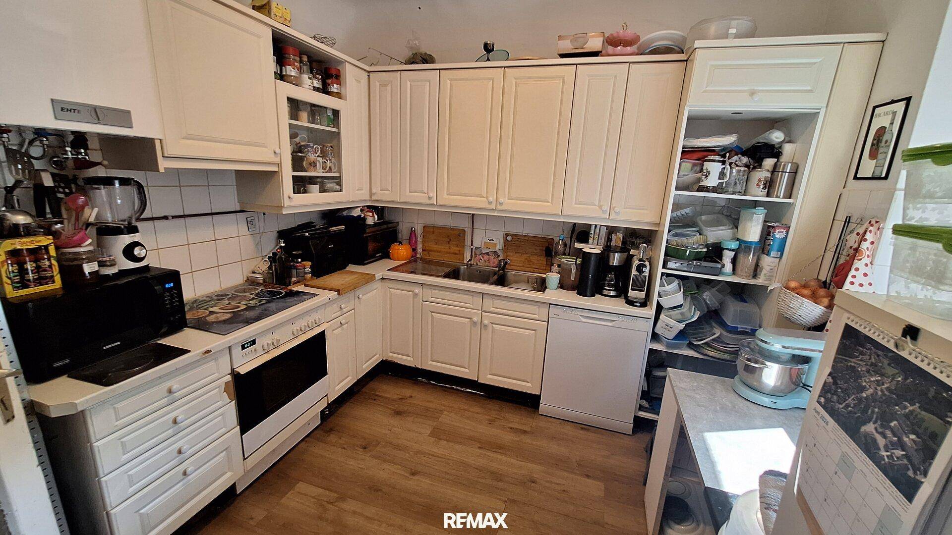 Funktionale Küche mit weißen Schränken, Herd, Backofen und vielen Küchengeräten.