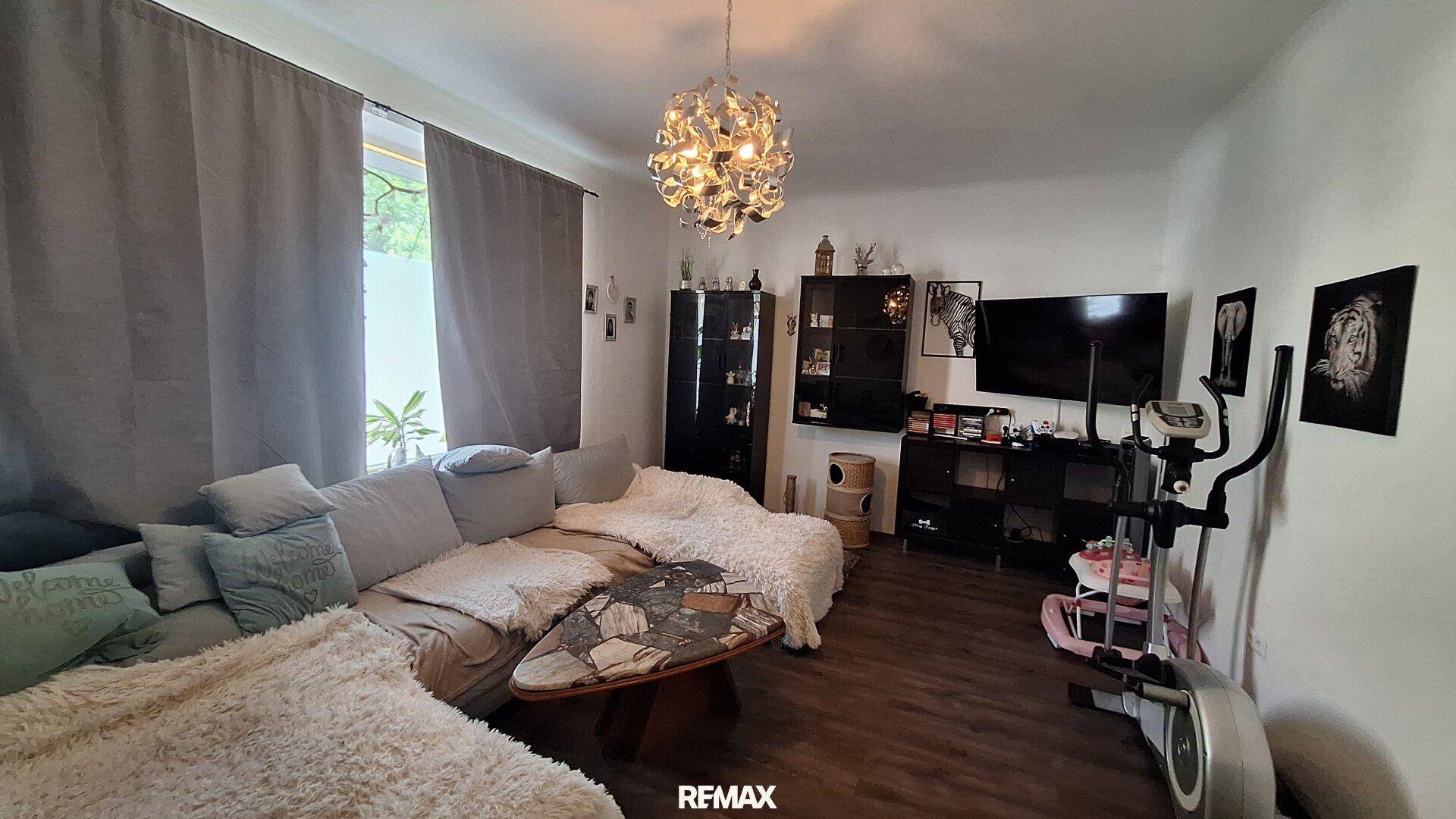 Gemütliches Wohnzimmer mit großem Ecksofa, Holzboden und einem Heimtrainer.