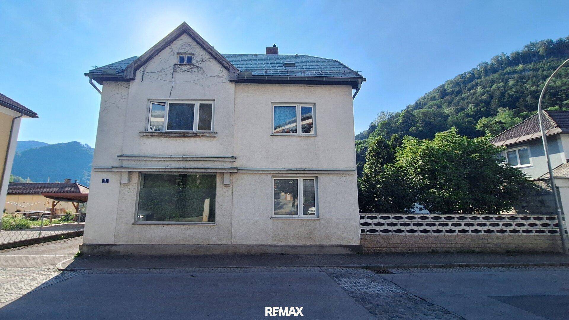 Vorderansicht eines freistehenden Hauses mit weißer Fassade und Satteldach an einer Straße.
