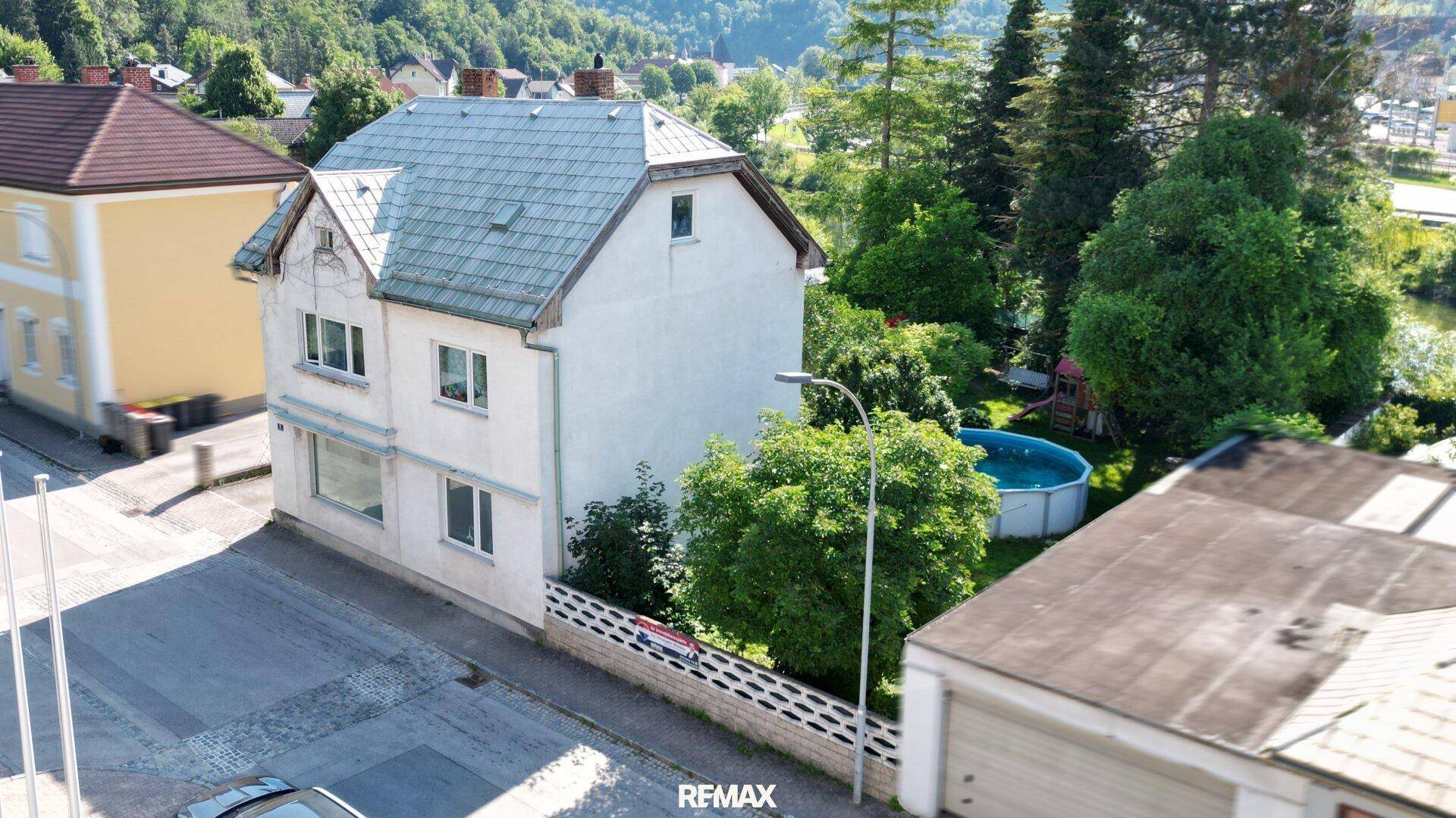Luftaufnahme eines Hauses mit Garten, Pool und angrenzender Straße in ländlicher Umgebung.