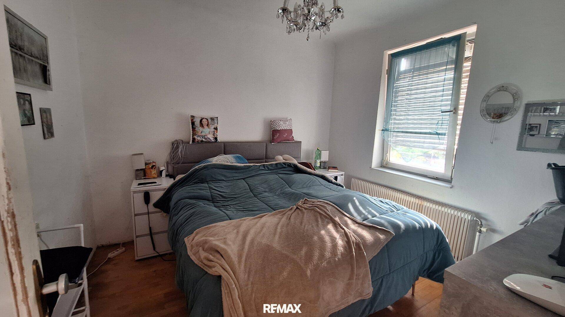 Schlafzimmer mit Doppelbett, Nachttischen und einem Fenster mit Jalousien.