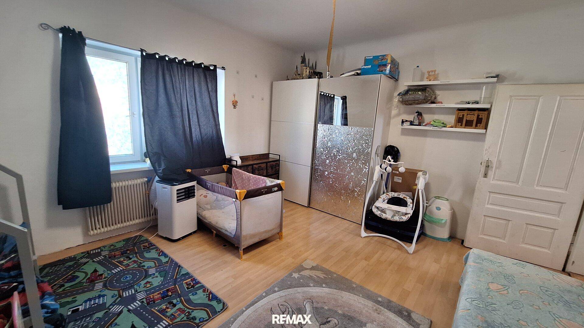 Kinderzimmer mit Babybett, Kleiderschrank, Spielteppichen und Fenster.