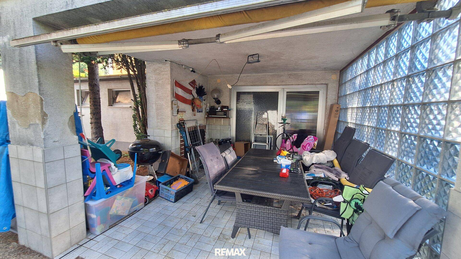 Überdachte Terrasse mit Esstisch, Stühlen und Grill, ideal für Mahlzeiten im Freien.