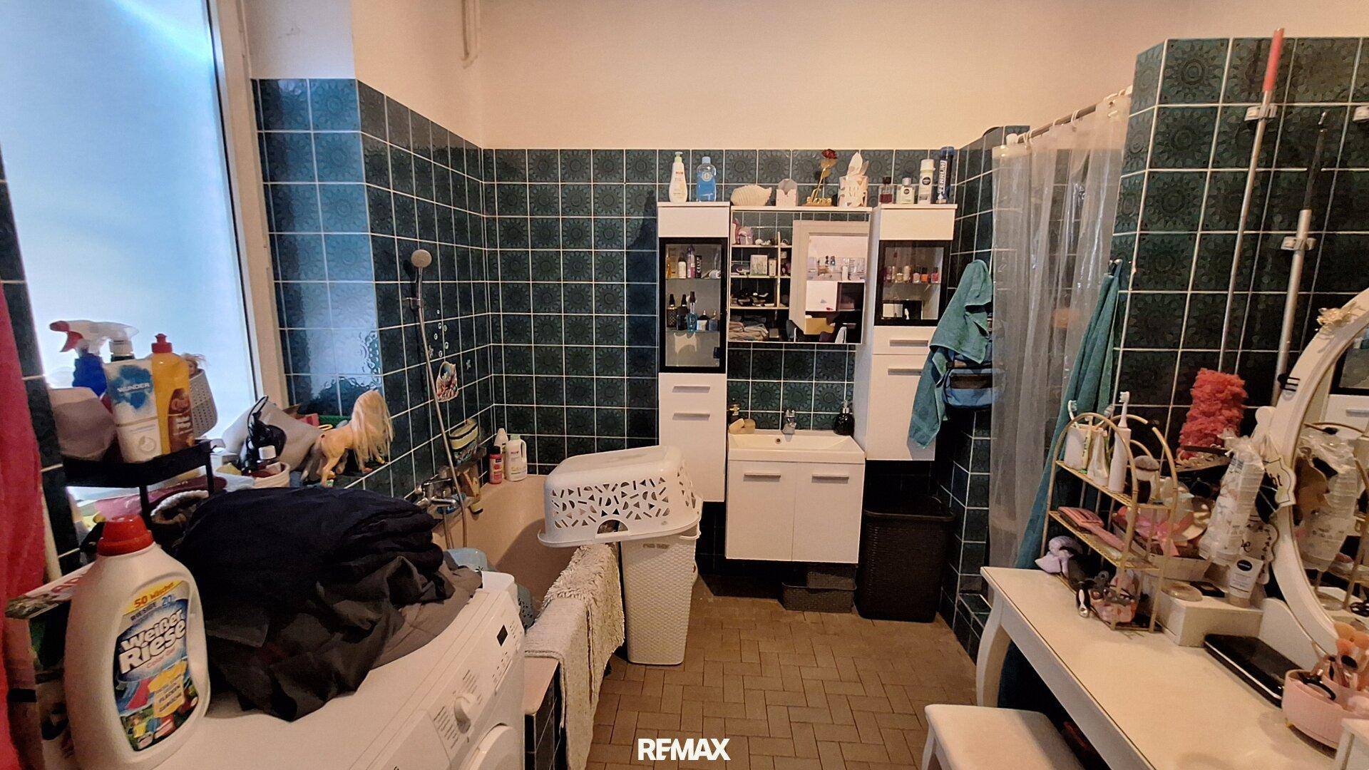 Badezimmer mit dunkelgrünen Fliesen, Badewanne, Waschmaschine und Fenster.