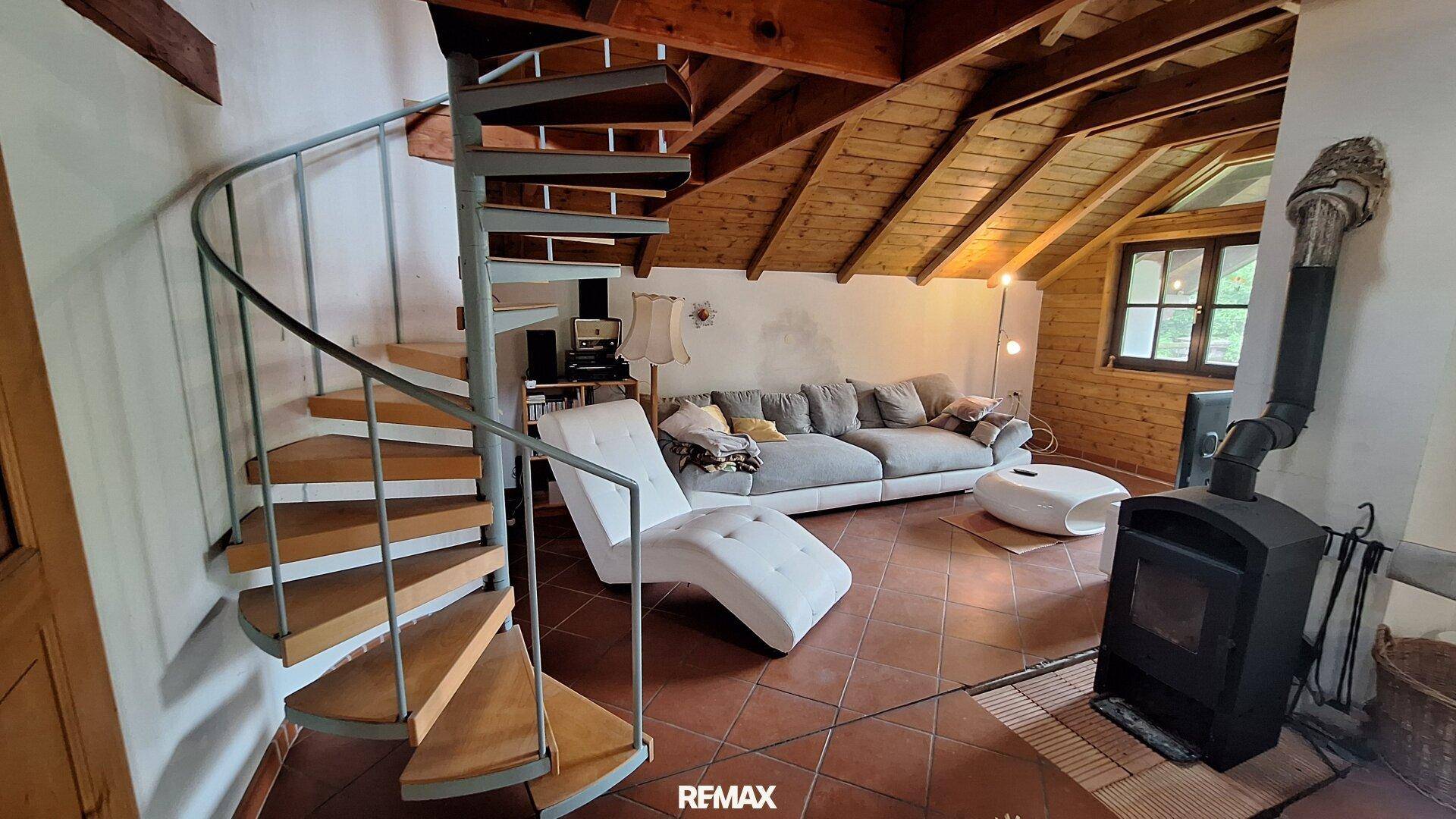 Gemütliches Wohnzimmer im Dachgeschoss mit Wendeltreppe, Holzbalken und Kaminofen.