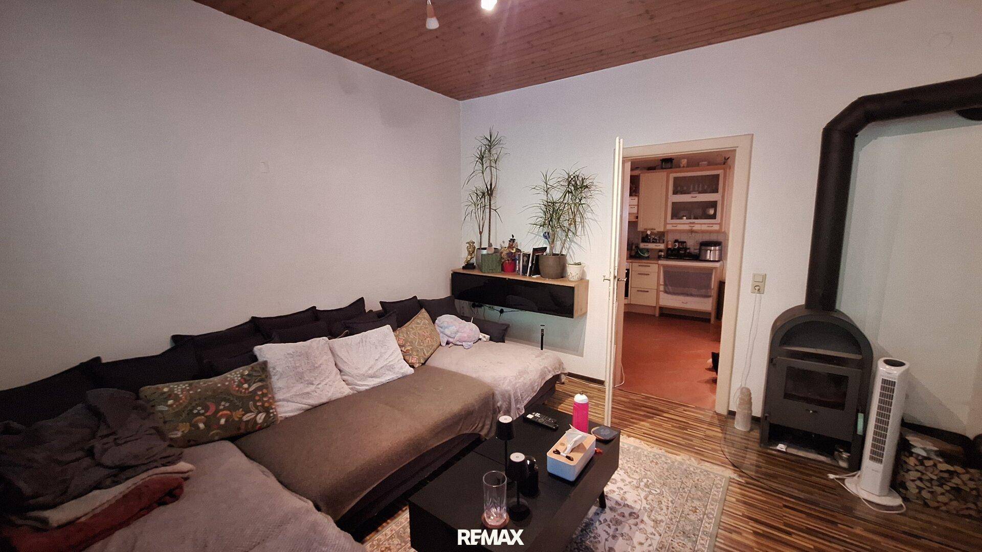 Wohnzimmer mit Holzboden, Kaminofen und Blick in die angrenzende Küche.