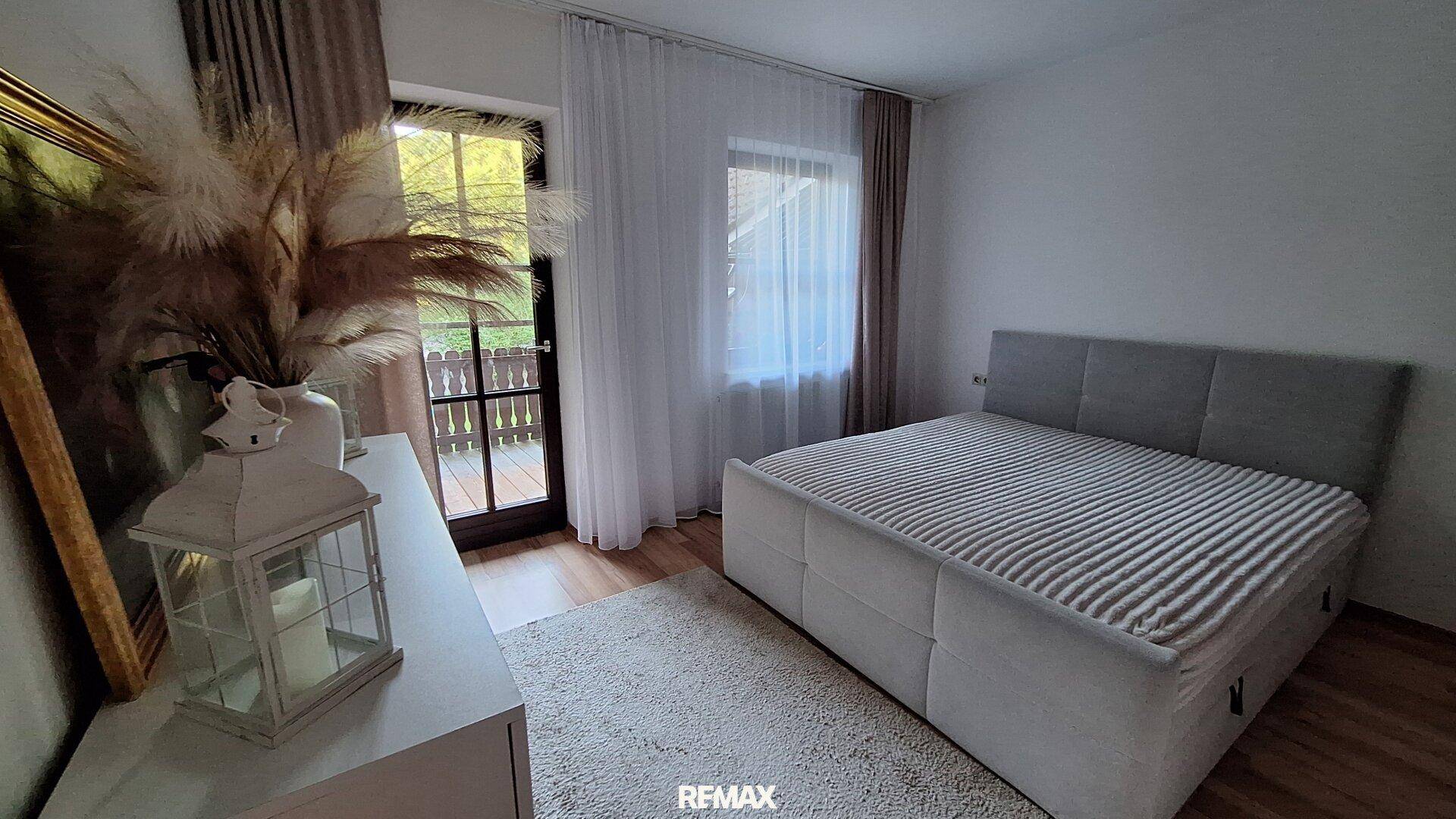 Helles Schlafzimmer mit Doppelbett, Teppichboden und Zugang zum Balkon.