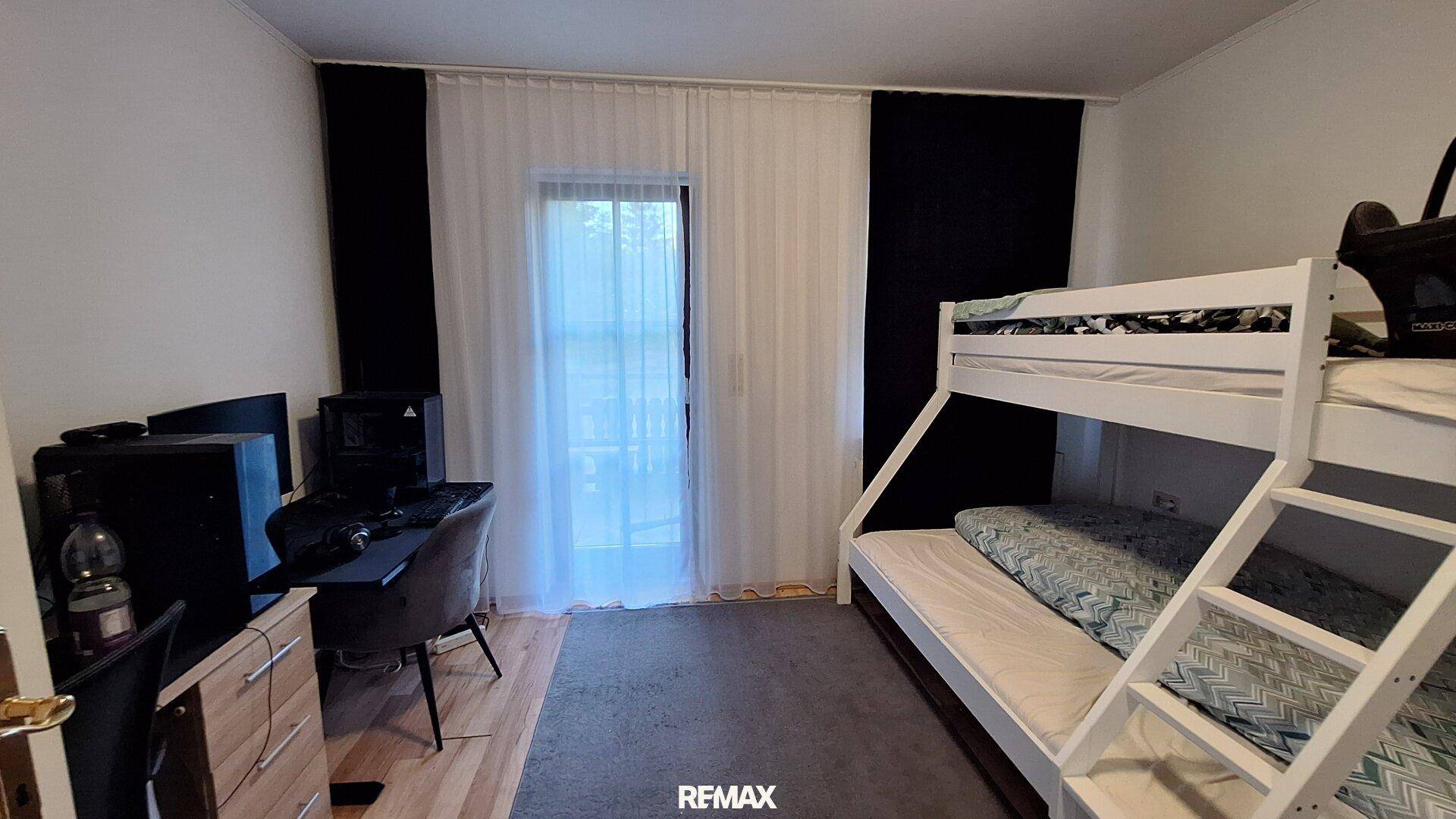 Kinderzimmer mit Etagenbett, Schreibtisch und Zugang zu einem Balkon.