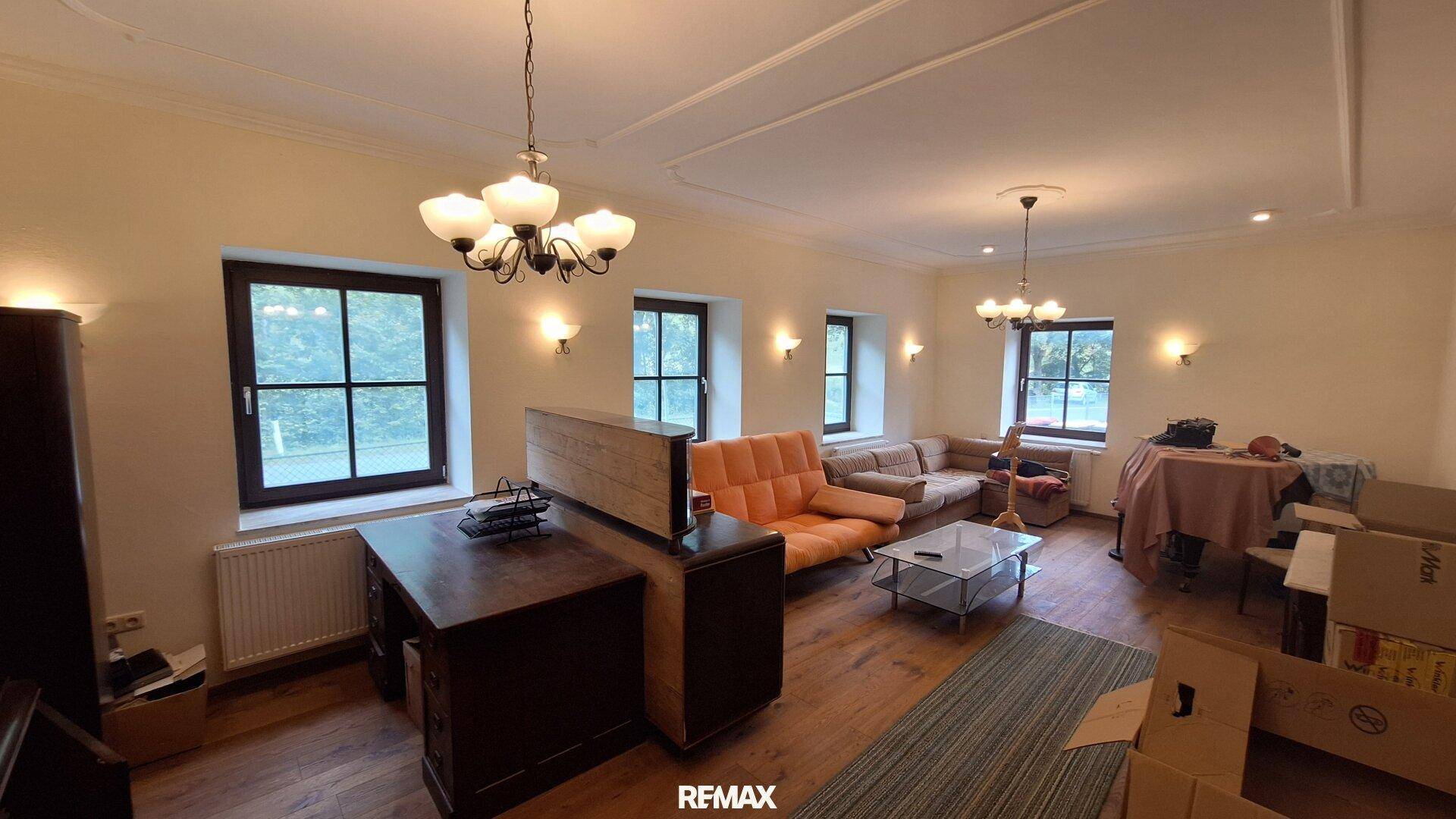 Geräumiges Wohnzimmer mit Holzboden, Stuckdecke und mehreren Fenstern.
