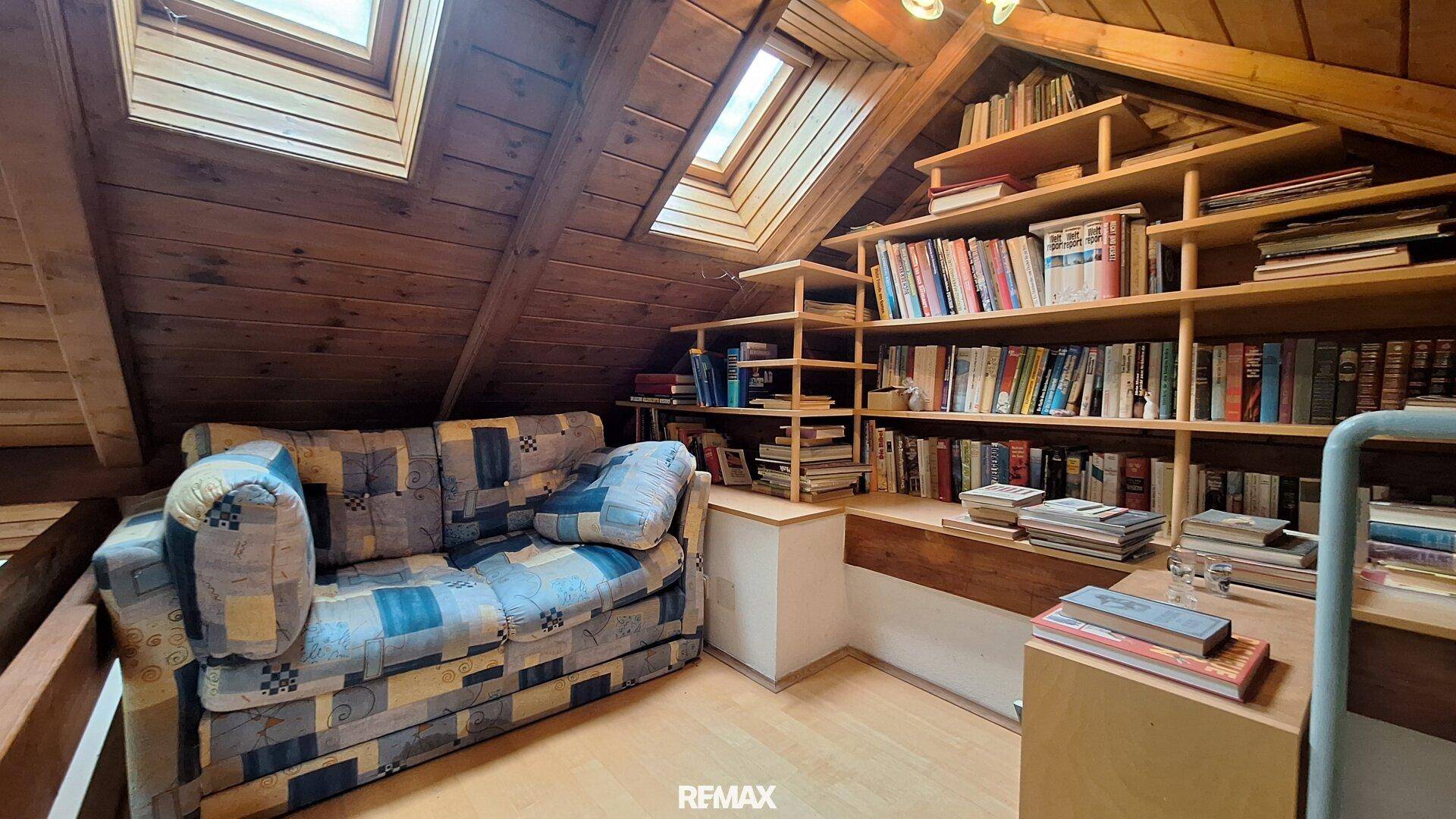 Gemütlicher Dachbodenbereich mit Sofa, Bücherregalen und Dachfenstern.
