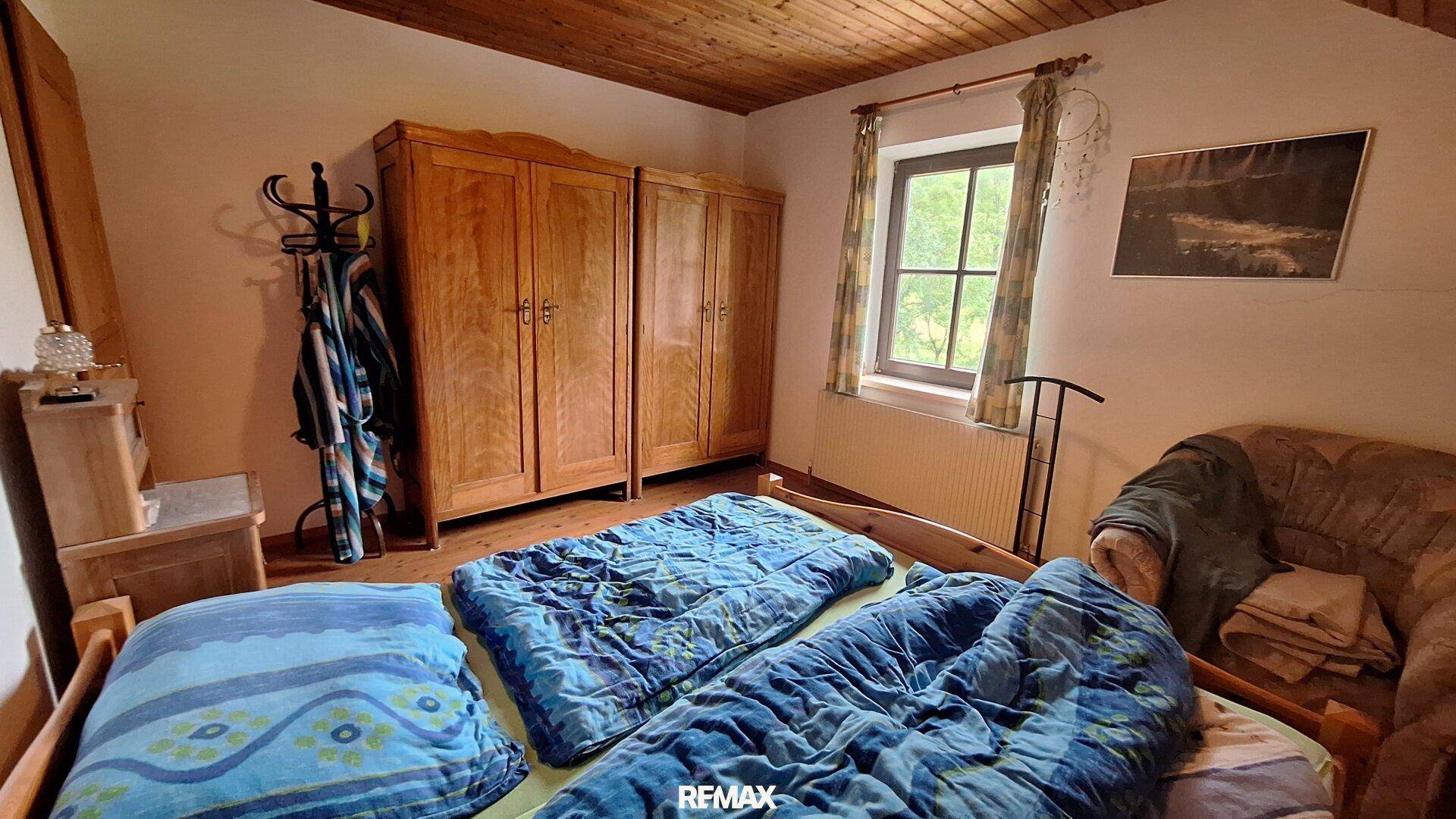 Schlafzimmer mit Holzboden, Holzschränken und Fenster mit Blick ins Grüne.