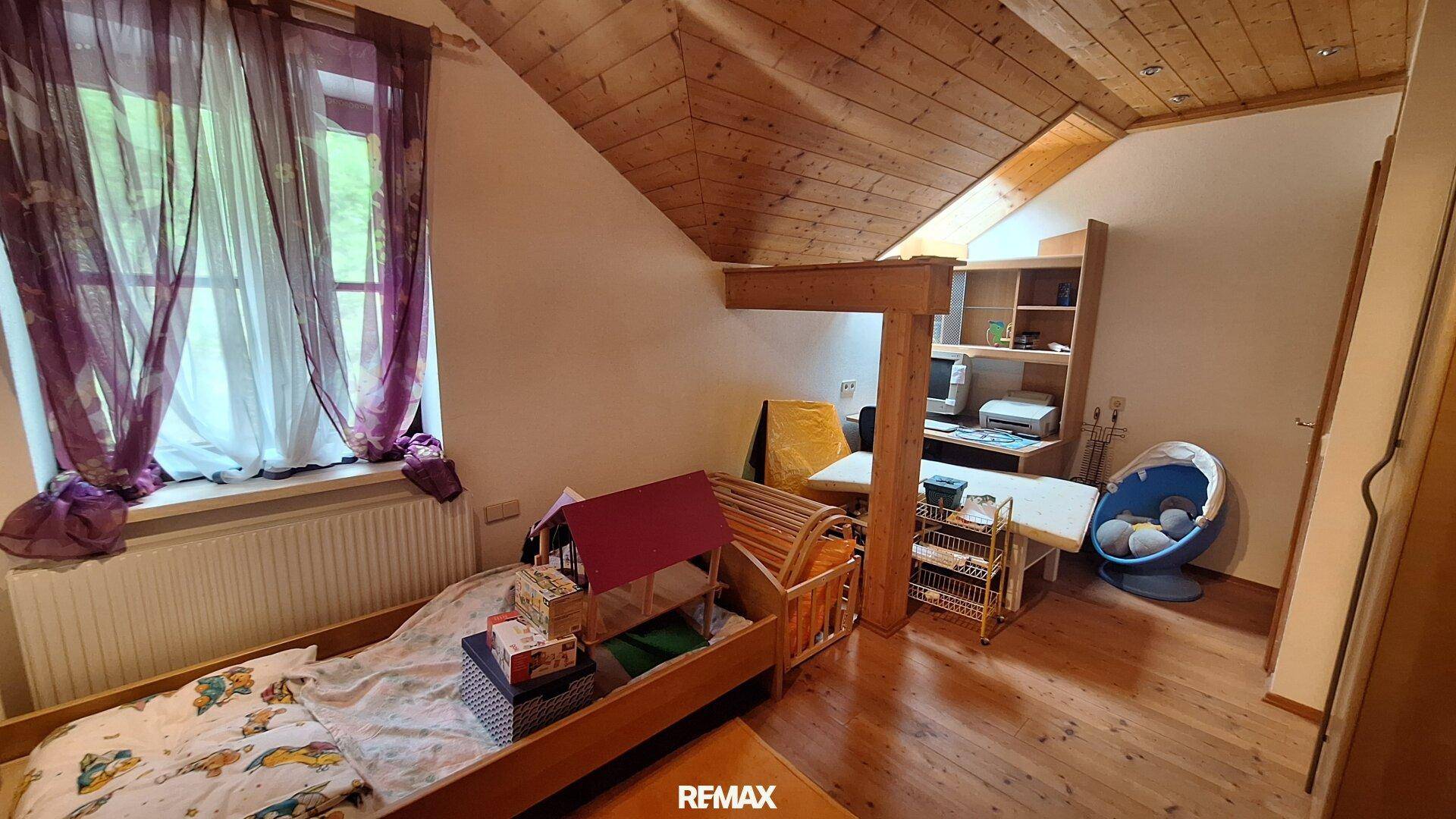Kinderzimmer im Dachgeschoss mit Holzboden, Holzwänden und Schreibtischbereich.