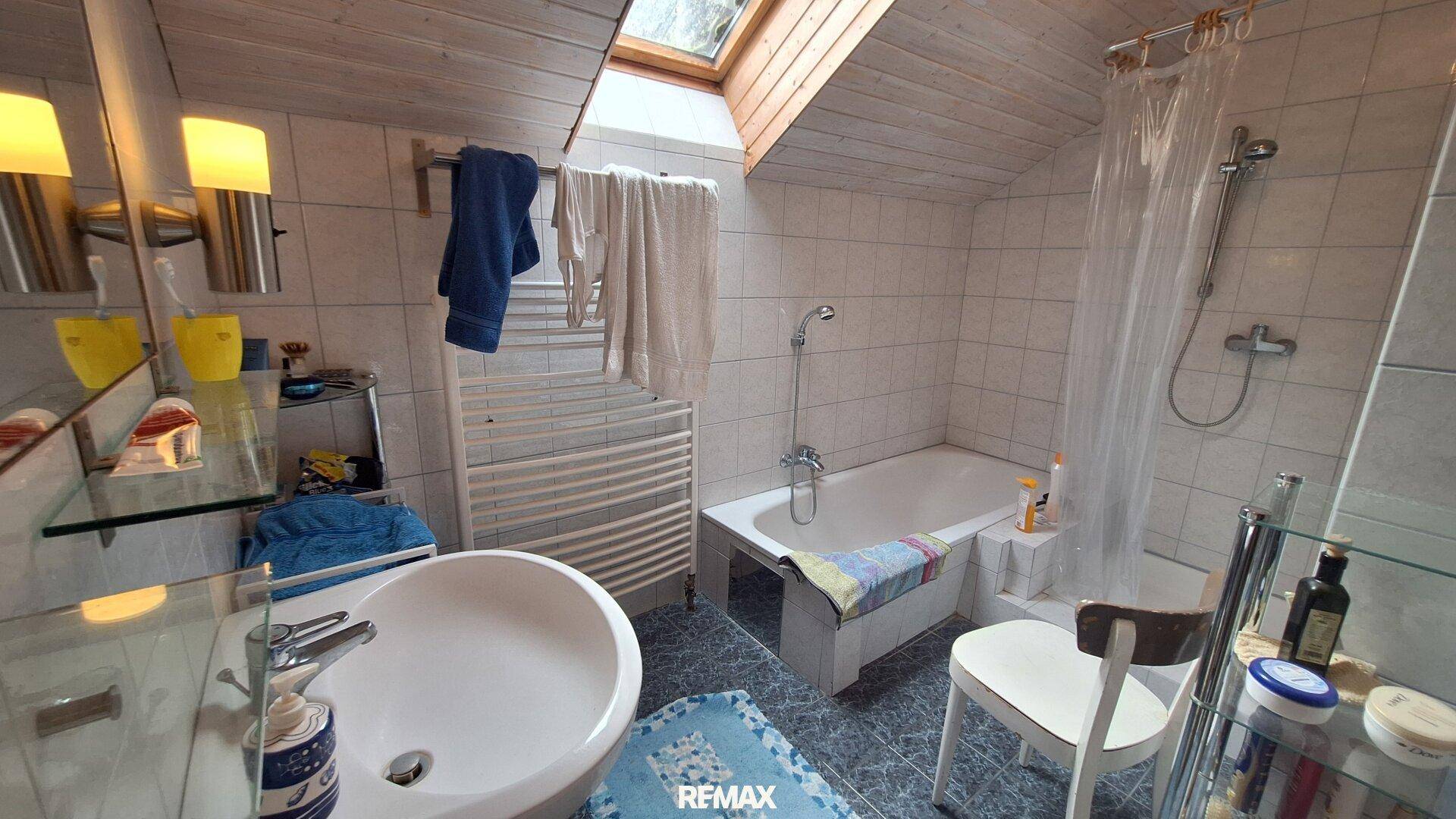 Helles Badezimmer im Dachgeschoss mit Badewanne, Waschbecken und Dachfenster.